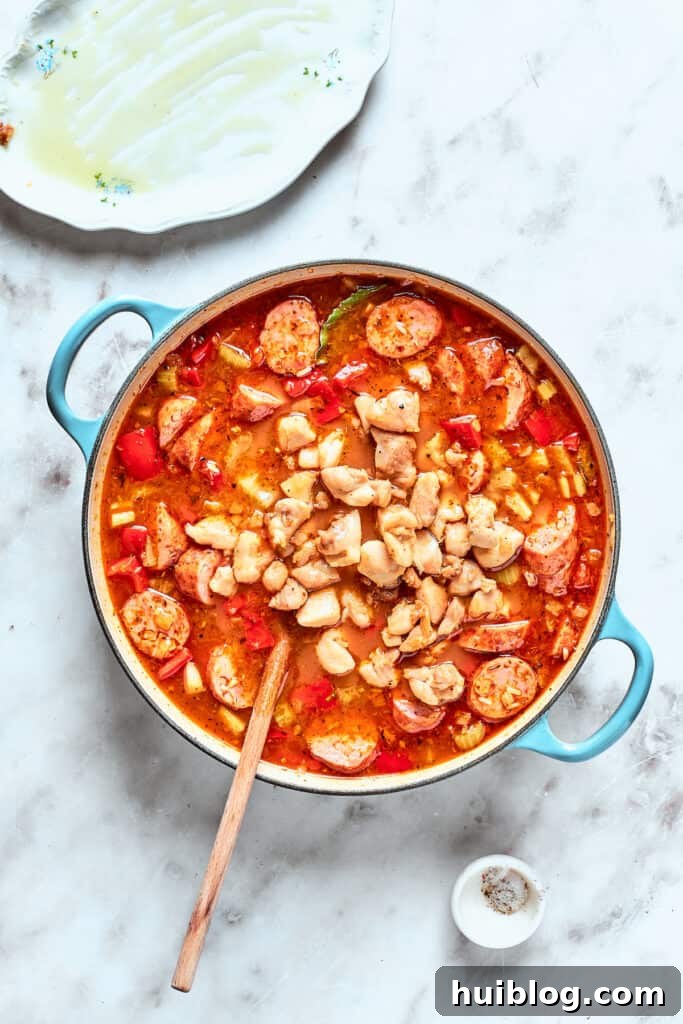 Cooked chicken pieces are returned to the pot with the simmering jambalaya mixture, ready to absorb more flavors.