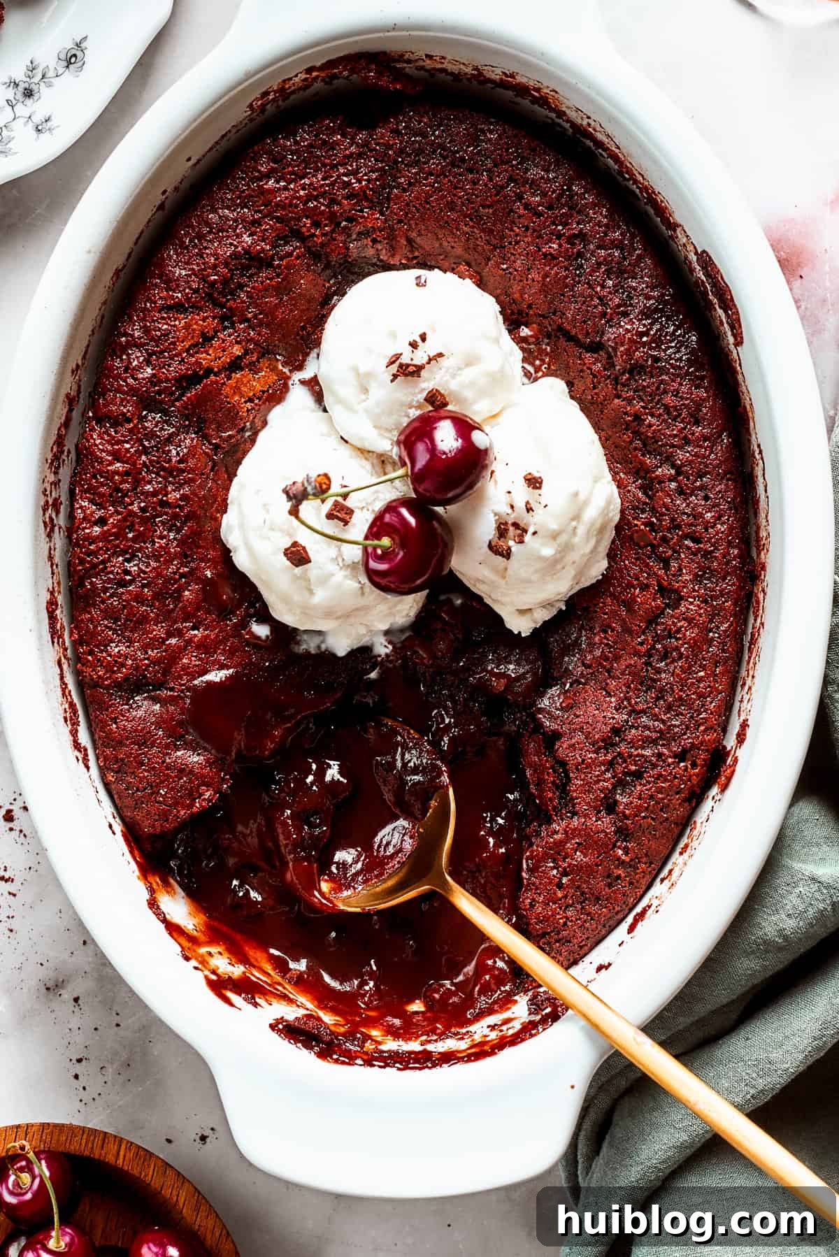An oval casserole dish with chocolate pudding cake topped with vanilla ice cream, with a spoon set in the pudding.