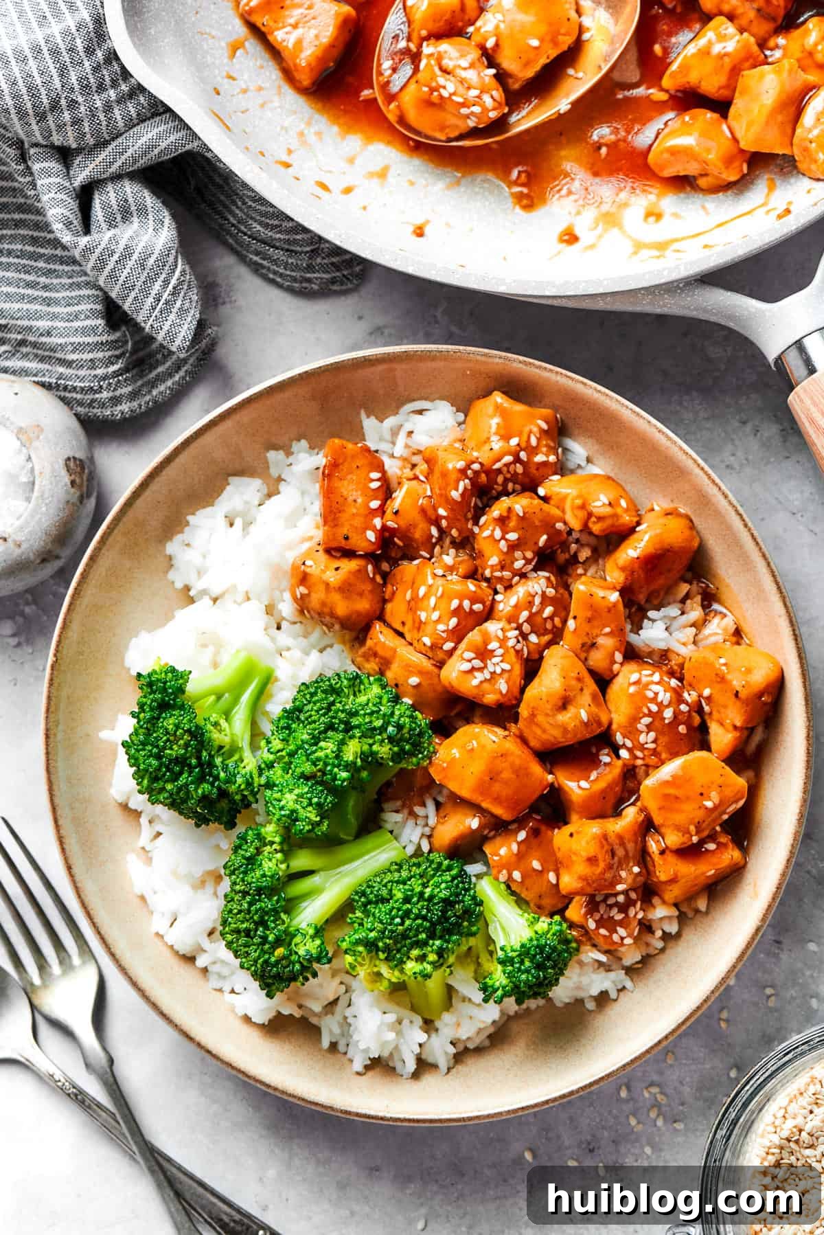 Perfectly Glazed Teriyaki Chicken 2 A bowl of rice is topped with teriyaki chicken and broccoli with more teriyaki chicken in the background.