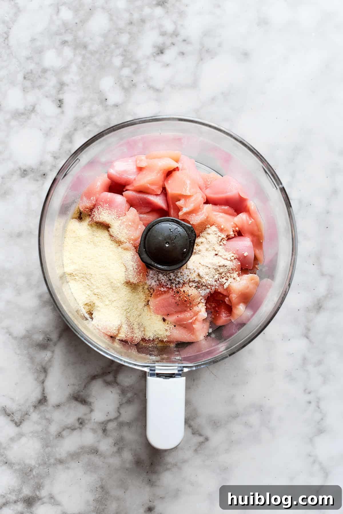 Chicken pieces, potato flakes, and spices are added to a food processor bowl, ready for blending.