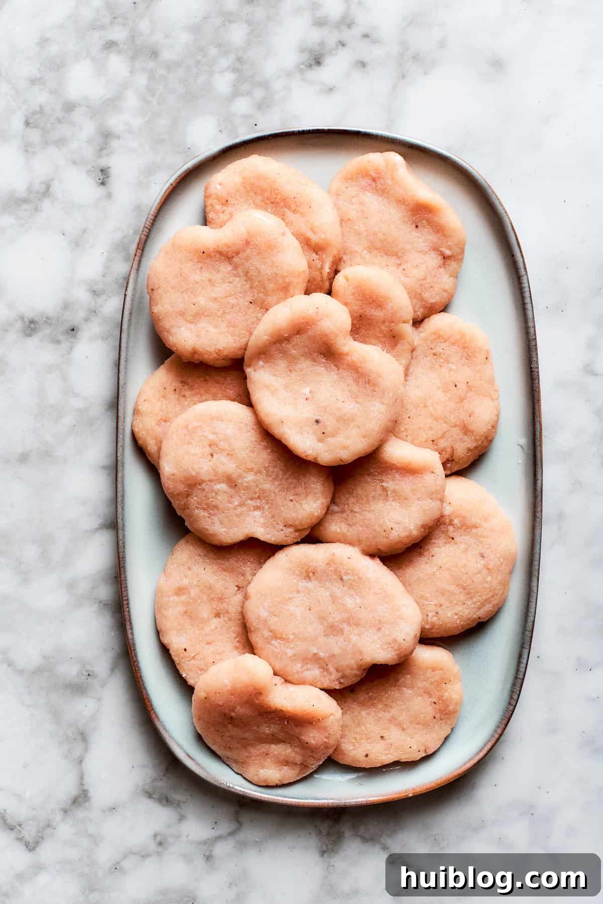 Small, uniformly shaped chicken nuggets are arranged on a plate, ready for breading.
