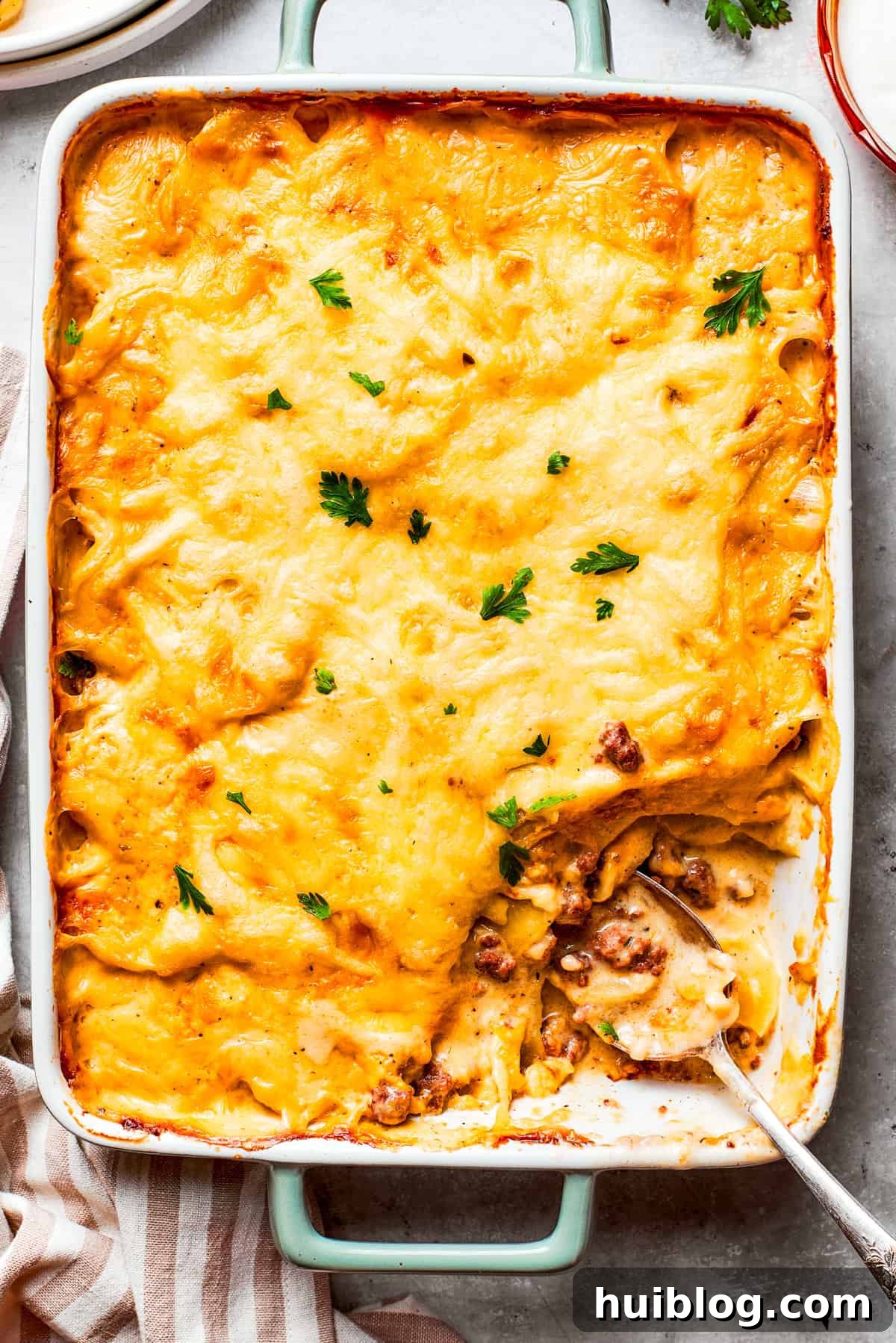 Overhead image of hamburger potato casserole in a baking dish, with a serving of it missing from the corner. The dish is golden brown and bubbling.