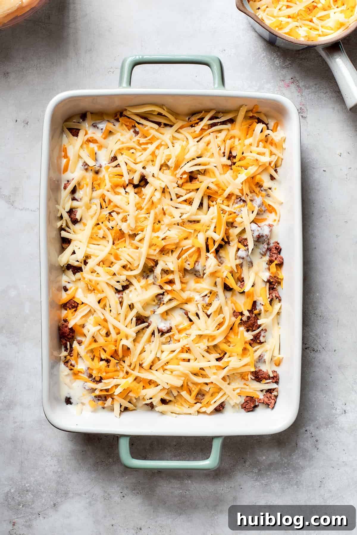 Hearty Ground Beef and Potato Bake 8 Shredded Colby Jack cheese is evenly sprinkled over a layer of ground beef in the casserole dish.