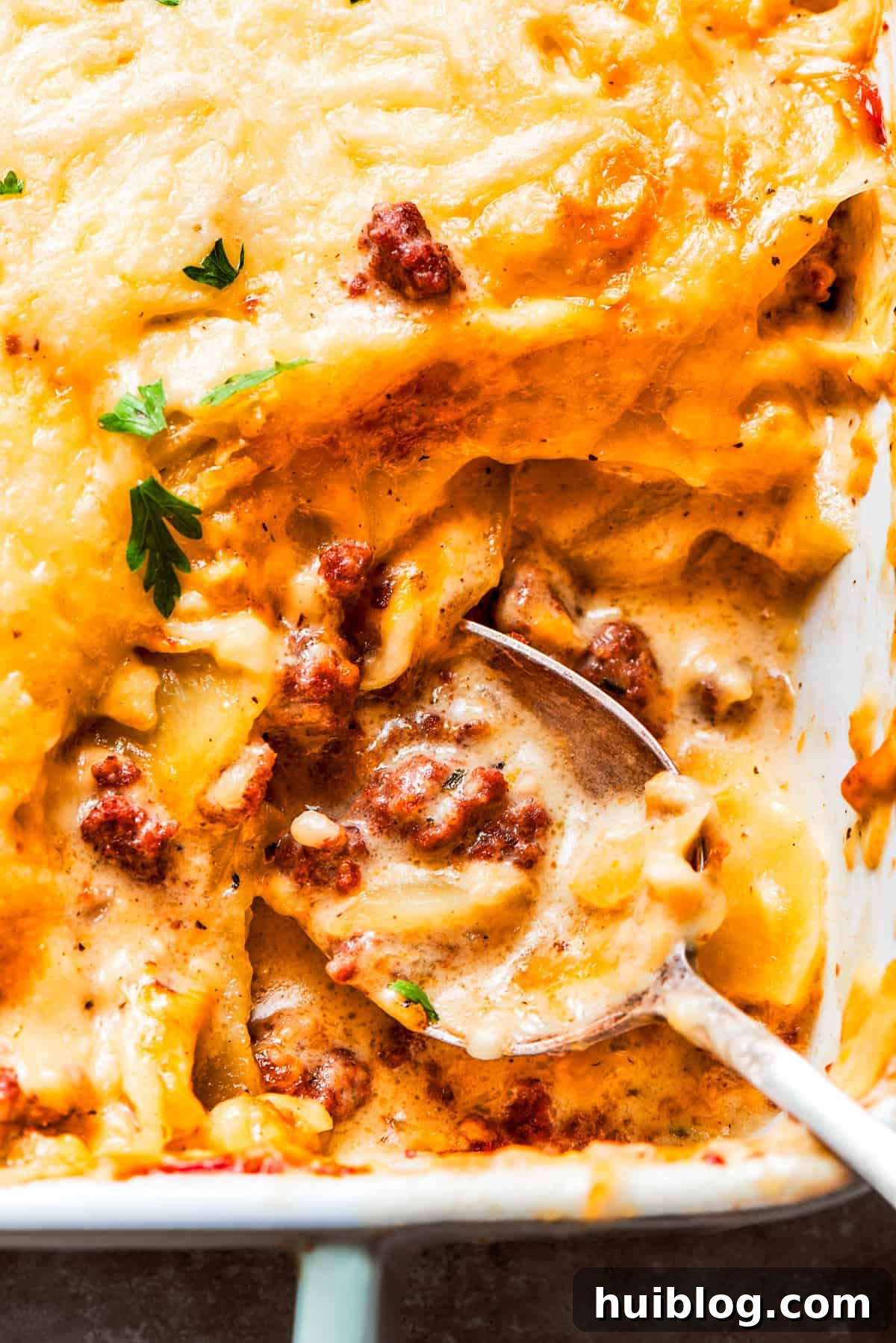 A spoon mixing through a casserole with ground beef and potatoes, highlighting the rich, creamy consistency.