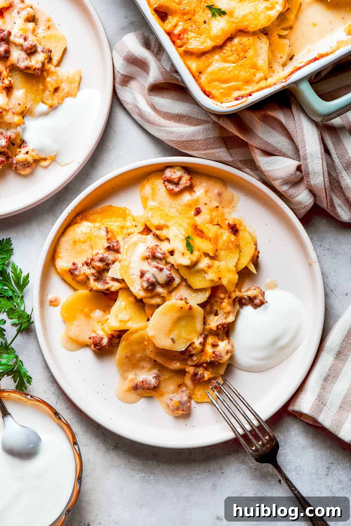 A family-favorite Hamburger Potato Casserole, served on dinner plates, offering creamy layers of beef, potatoes, and melted cheese. A serving of creamy hamburger potato casserole on a dinner plate, garnished with fresh parsley, ready to be enjoyed.
