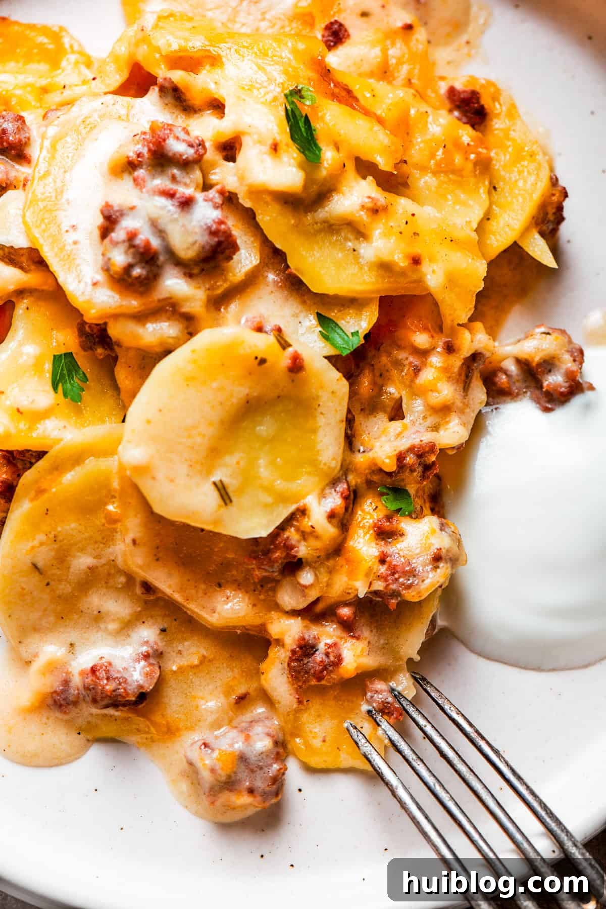 Close-up image of cooked sliced potatoes and ground beef served on a dinner plate with a fork set next to the food, ready to eat.