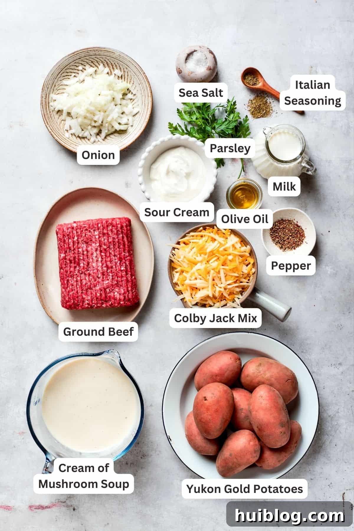 Essential ingredients for a delicious Hamburger Potato Casserole, including mushroom soup, yellow potatoes, savory ground beef, and melted cheese. Ingredients for creamy hamburger potato casserole: ground beef, shredded Colby Jack cheese, chopped onion, sour cream, salt, pepper, milk, Italian seasoning, cream of mushroom soup, and Yukon gold potatoes.