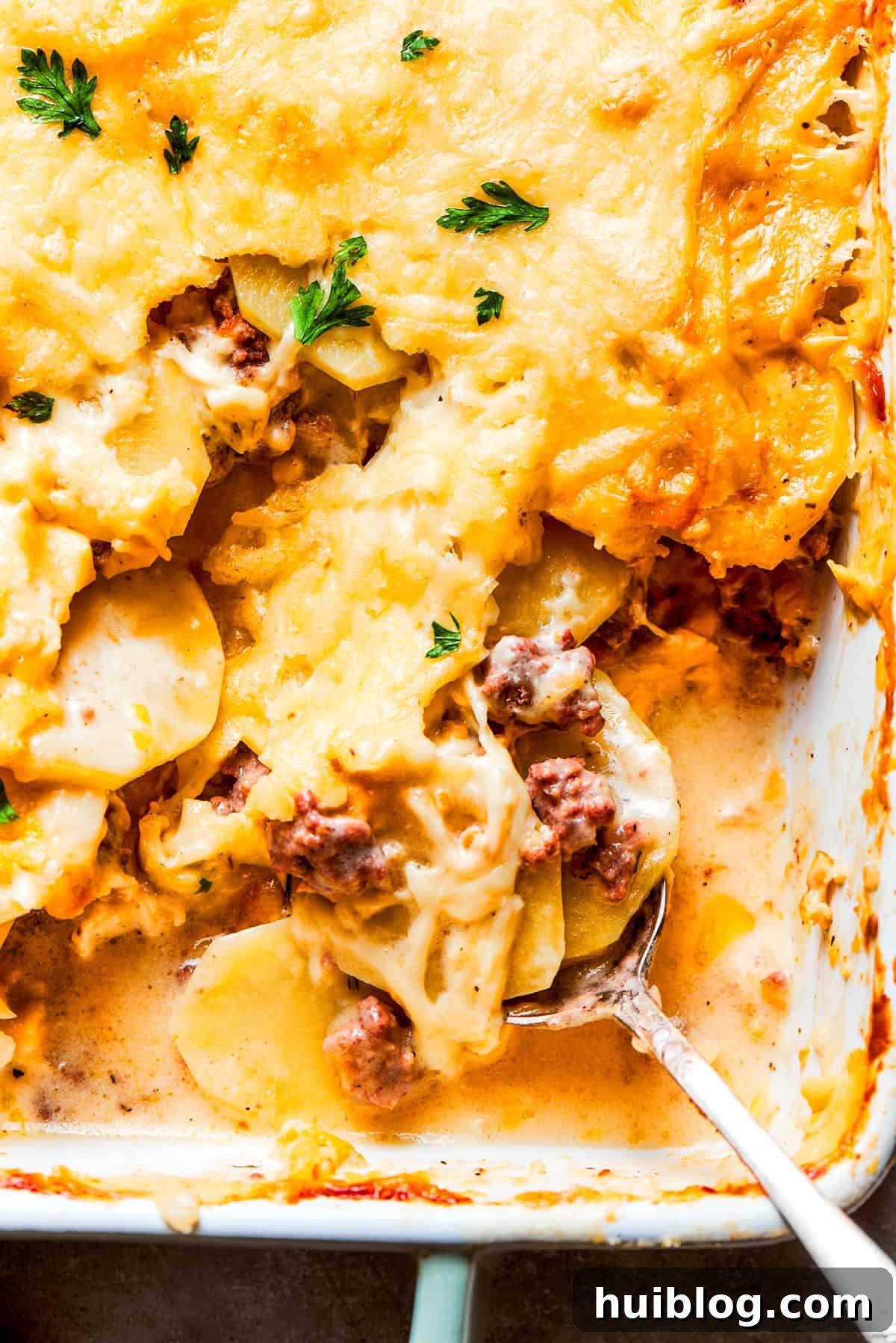 Up close photo of a spoon mixing through a casserole with ground beef and potatoes, showing the creamy texture and layers.