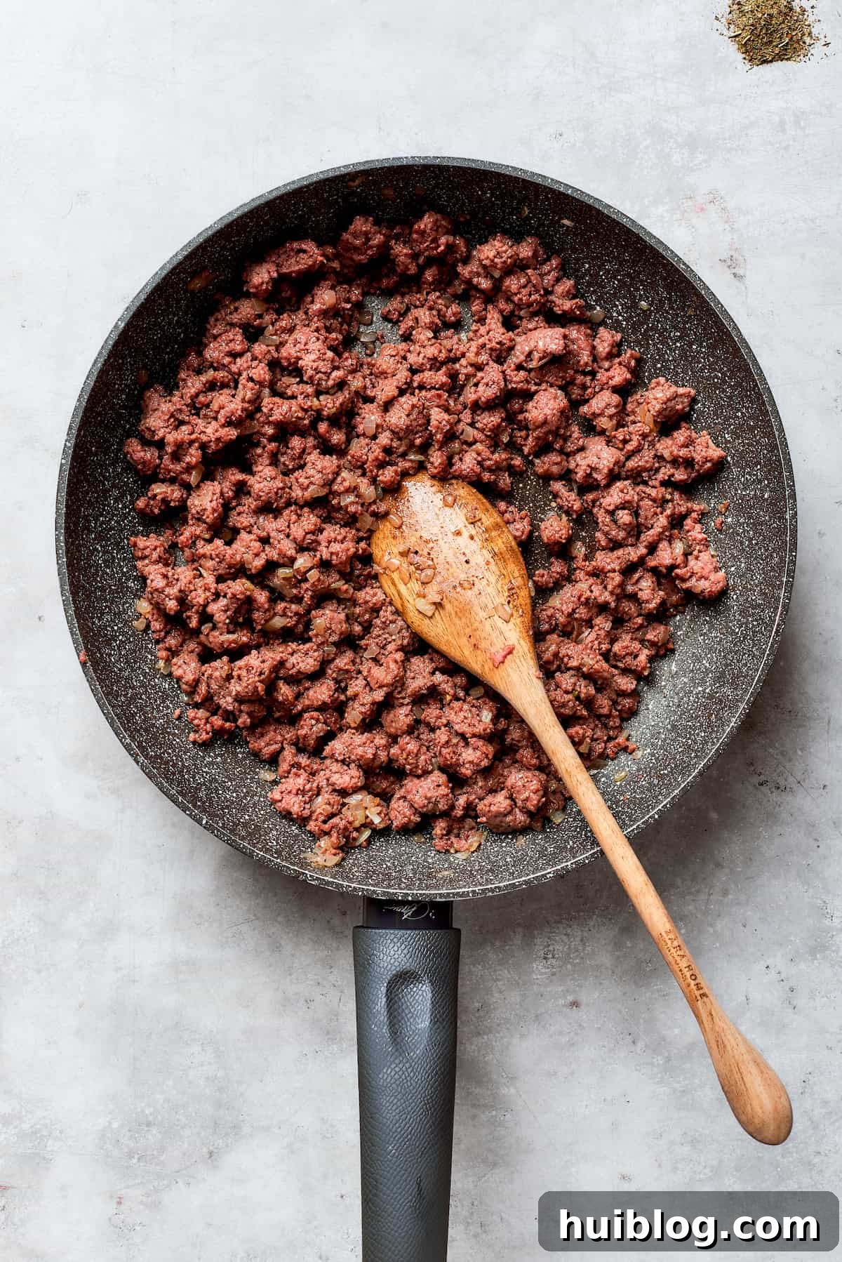Hearty Ground Beef and Potato Bake 3 The ground beef is browning in a skillet with chopped onions, releasing savory aromas.