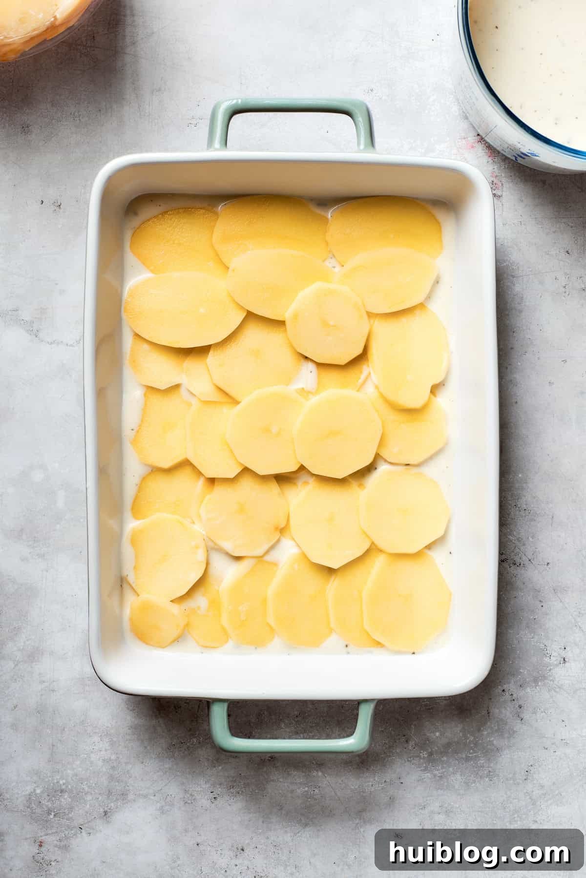 Hearty Ground Beef and Potato Bake 7 Neatly sliced potatoes are arranged in a single layer on the bottom of the greased baking pan.
