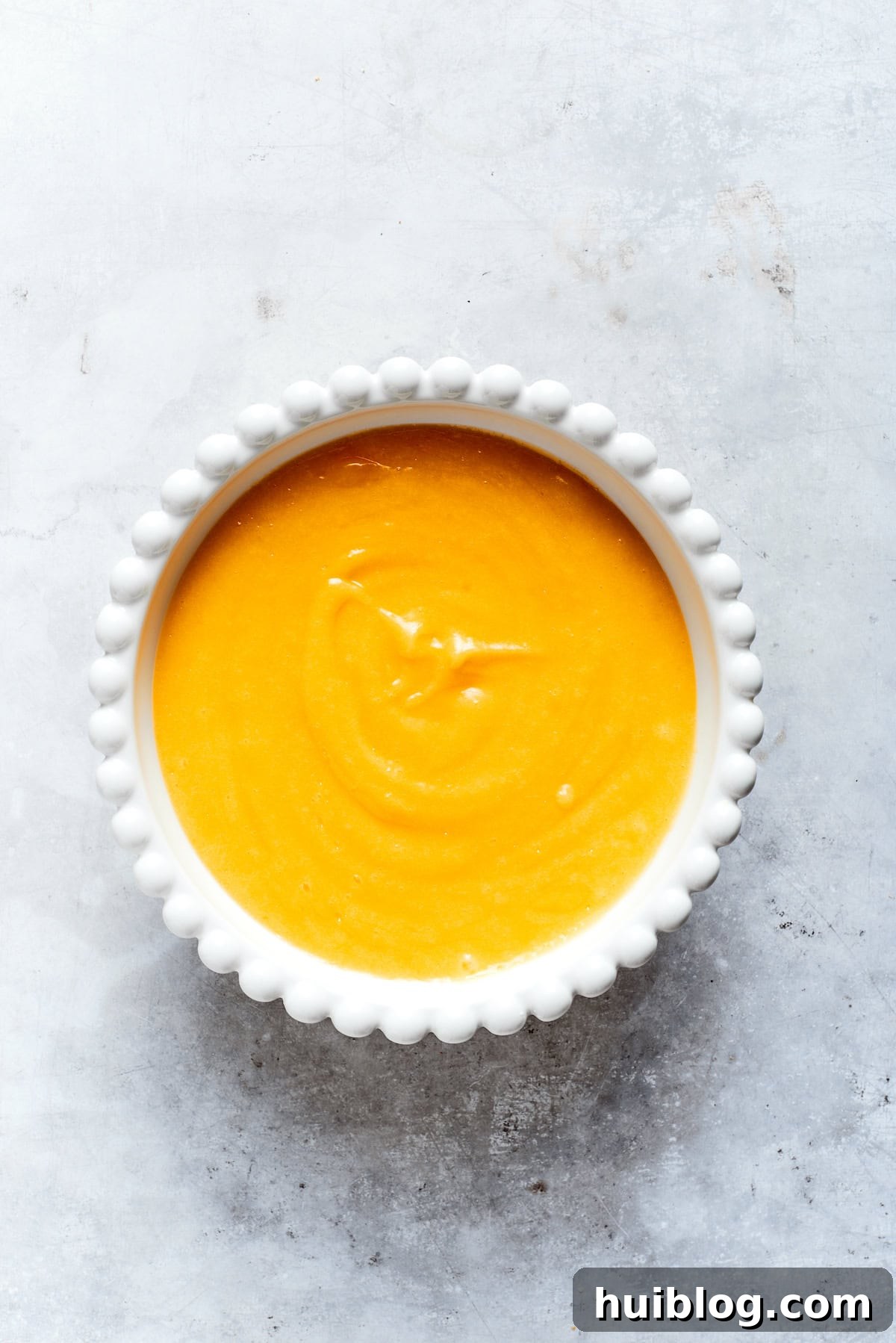 A bowl filled with freshly made, smooth, and vibrant yellow lemon curd.
