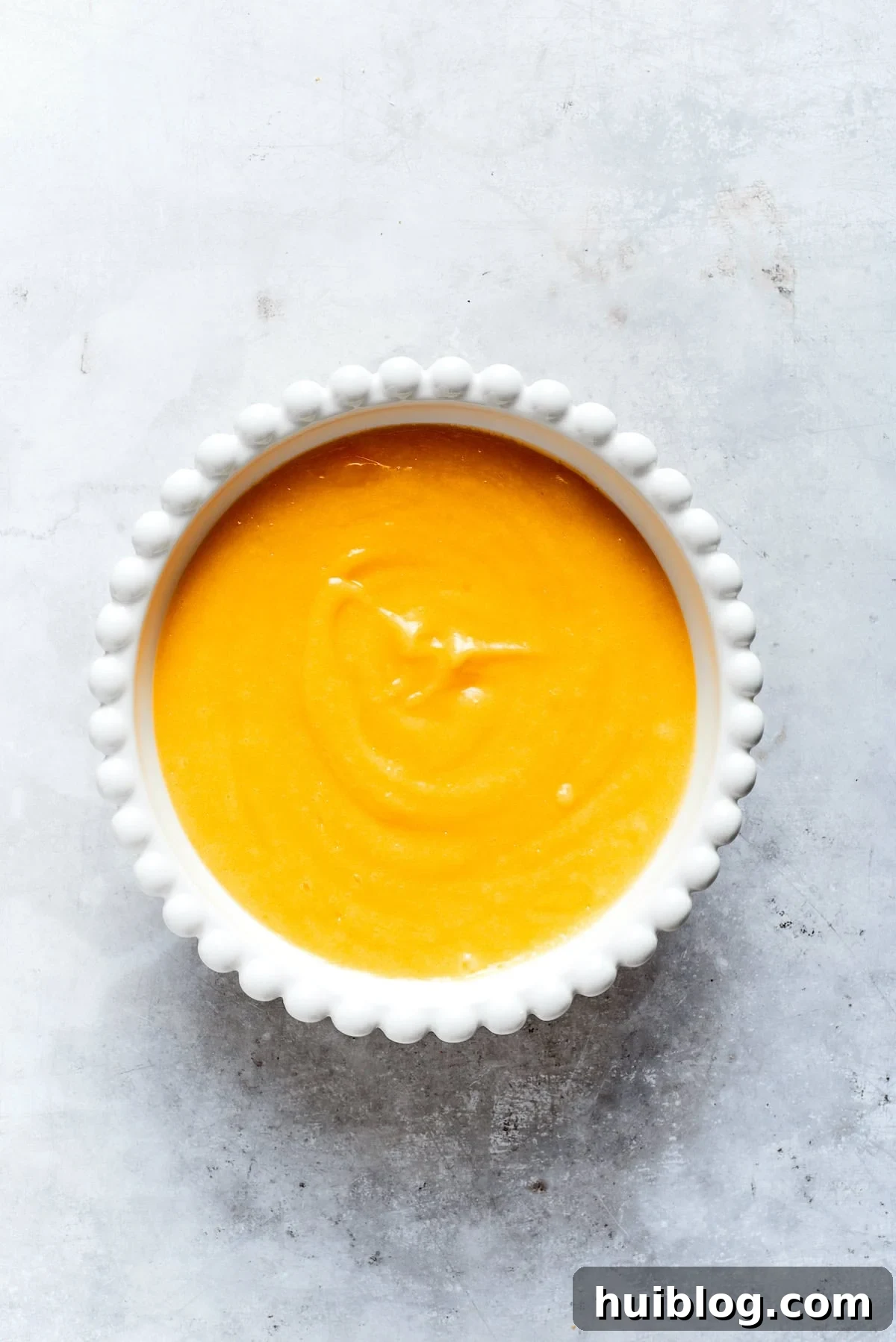 Smooth, vibrant yellow lemon curd is cooling in a glass bowl after being perfectly cooked and strained.