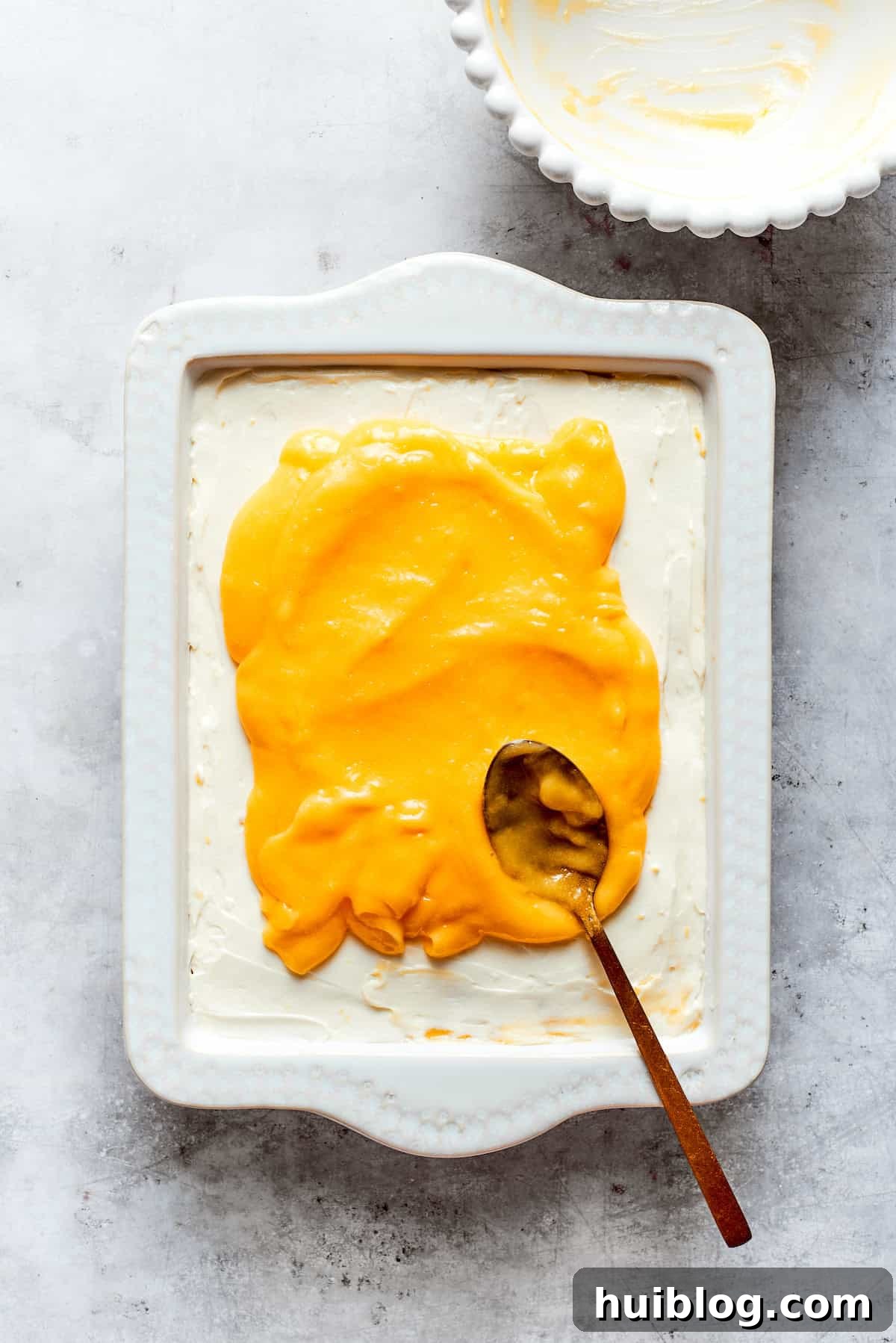 The final layer of smooth, bright lemon curd is spread over the mascarpone cream, completing the tiramisu assembly.