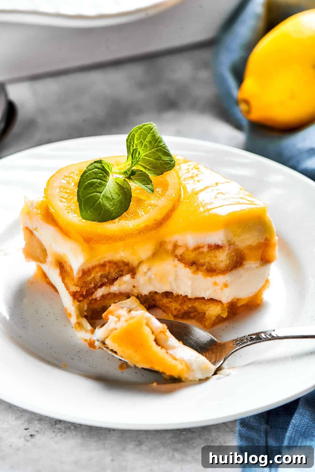 A fork taking a bite out of a creamy portion of lemon tiramisu, served on a delicate dessert plate.