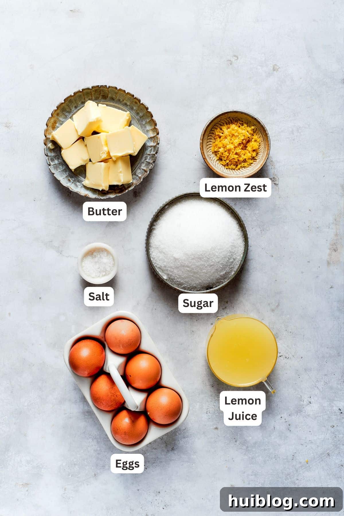 Lemon curd ingredients carefully arranged: butter, fresh eggs, granulated sugar, lemon juice, lemon zest, and a pinch of salt.