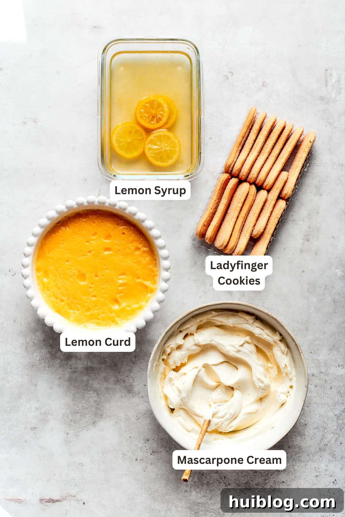 All components of lemon tiramisu ready for assembly: ladyfinger cookies, homemade lemon curd, mascarpone cream filling, and lemon syrup.