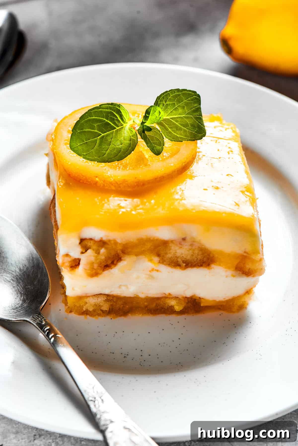 A perfectly cut square of lemon tiramisu adorned with a fresh basil leaf on a white plate, ready to be enjoyed.