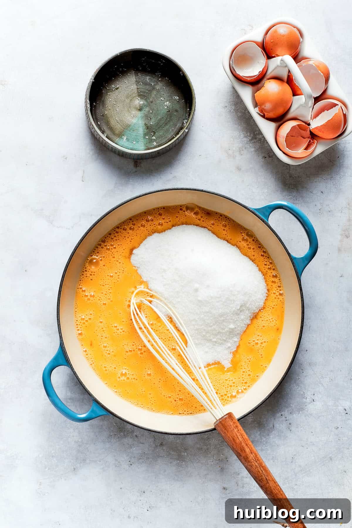 Granulated sugar being whisked vigorously into a bowl with eggs and lemon juice for the lemon curd base.