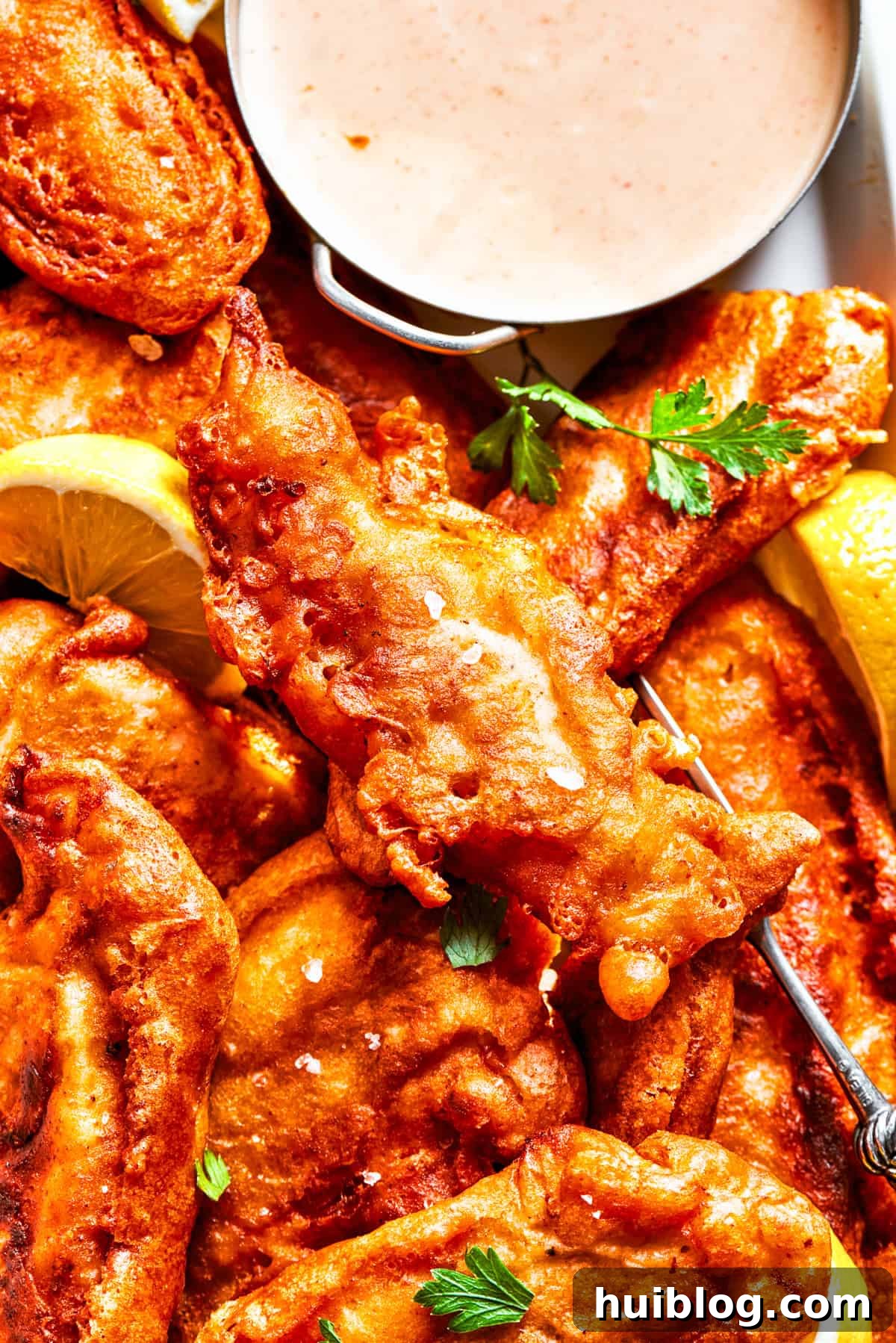 Light and crispy on the outside with a fork-tender inside, Beer Battered Chicken is an instant classic and so easy to make! Closeup photo of battered chicken arranged on a plate with a bowl of dipping sauce.
