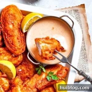 Crispy Ale-Coated Chicken Bites 2 A piece of beer battered chicken is dipped into spicy sauce with more chicken pieces around it.