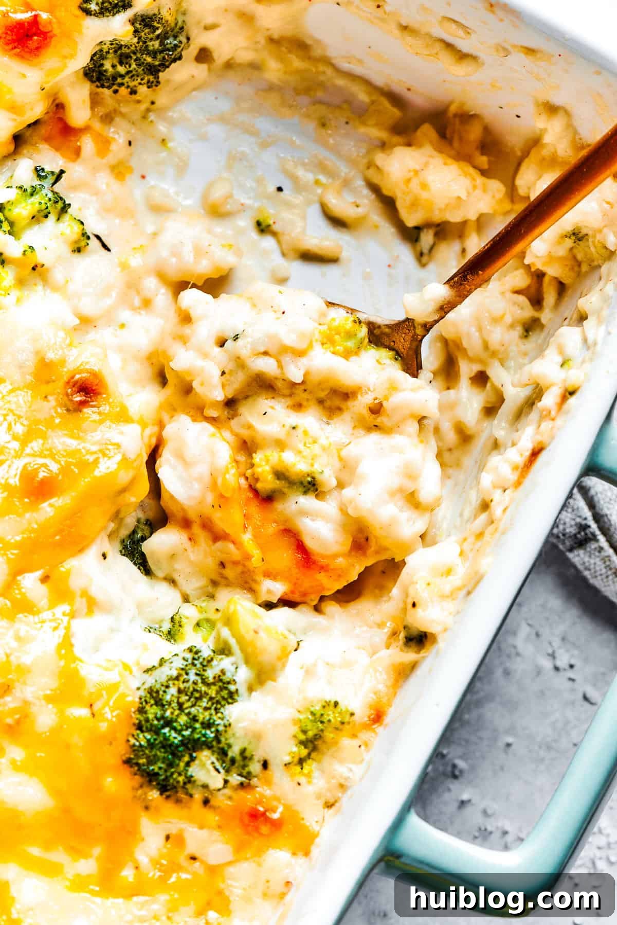 From-scratch Broccoli & Rice Casserole folds tender broccoli and fluffy white rice into a gorgeously creamy three-cheese sauce. A serving utensil scoops into a pan of golden-brown broccoli and rice casserole, highlighting the creamy texture and melted cheese.