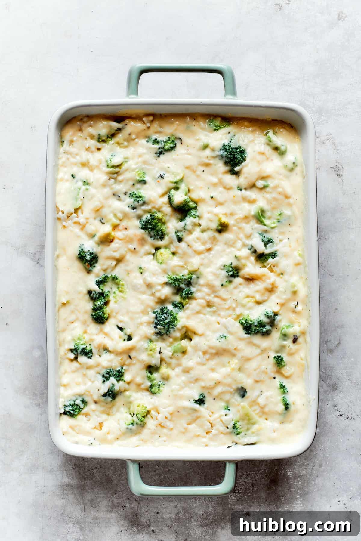 From-scratch Broccoli & Rice Casserole folds tender broccoli and fluffy white rice into a gorgeously creamy three-cheese sauce. Cooked broccoli florets and fluffy white rice are gently stirred into the creamy cheese sauce within a baking pan, ensuring an even distribution.