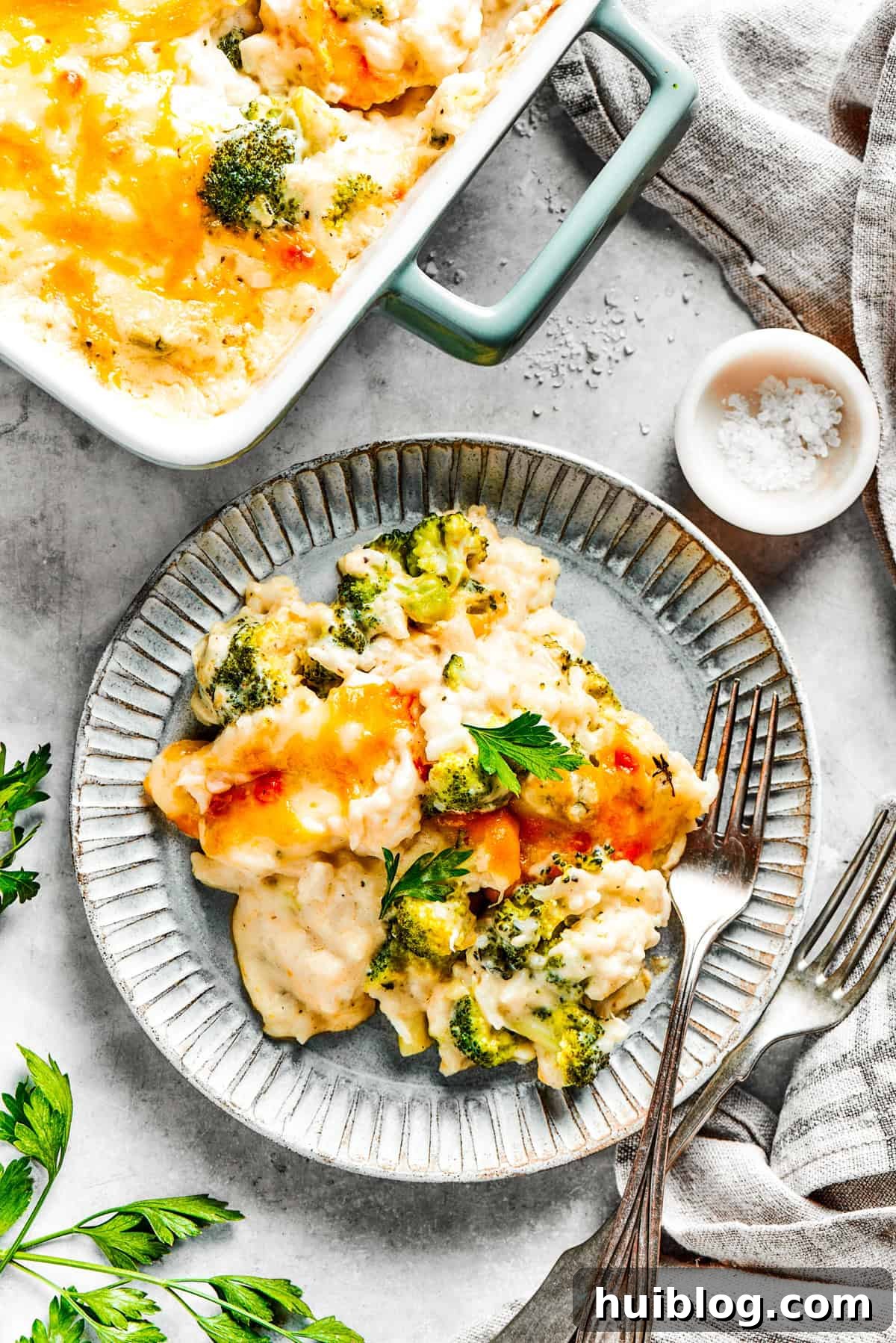 From-scratch Broccoli & Rice Casserole folds tender broccoli and fluffy white rice into a gorgeously creamy three-cheese sauce. A complete dinner plate featuring a hearty serving of cheesy broccoli rice casserole next to a main protein, demonstrating a delicious meal.