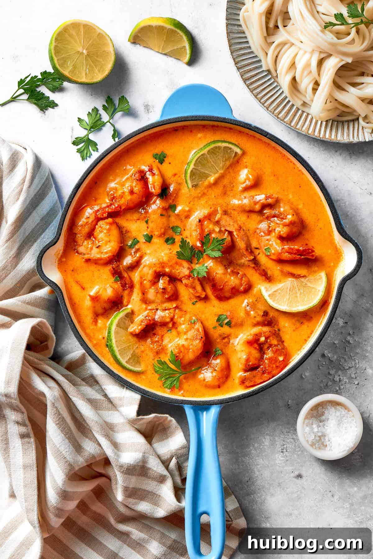 A skillet of cajun shrimp in tomato sauce, with lime wedges placed around the shrimp and a garnish of fresh herbs.