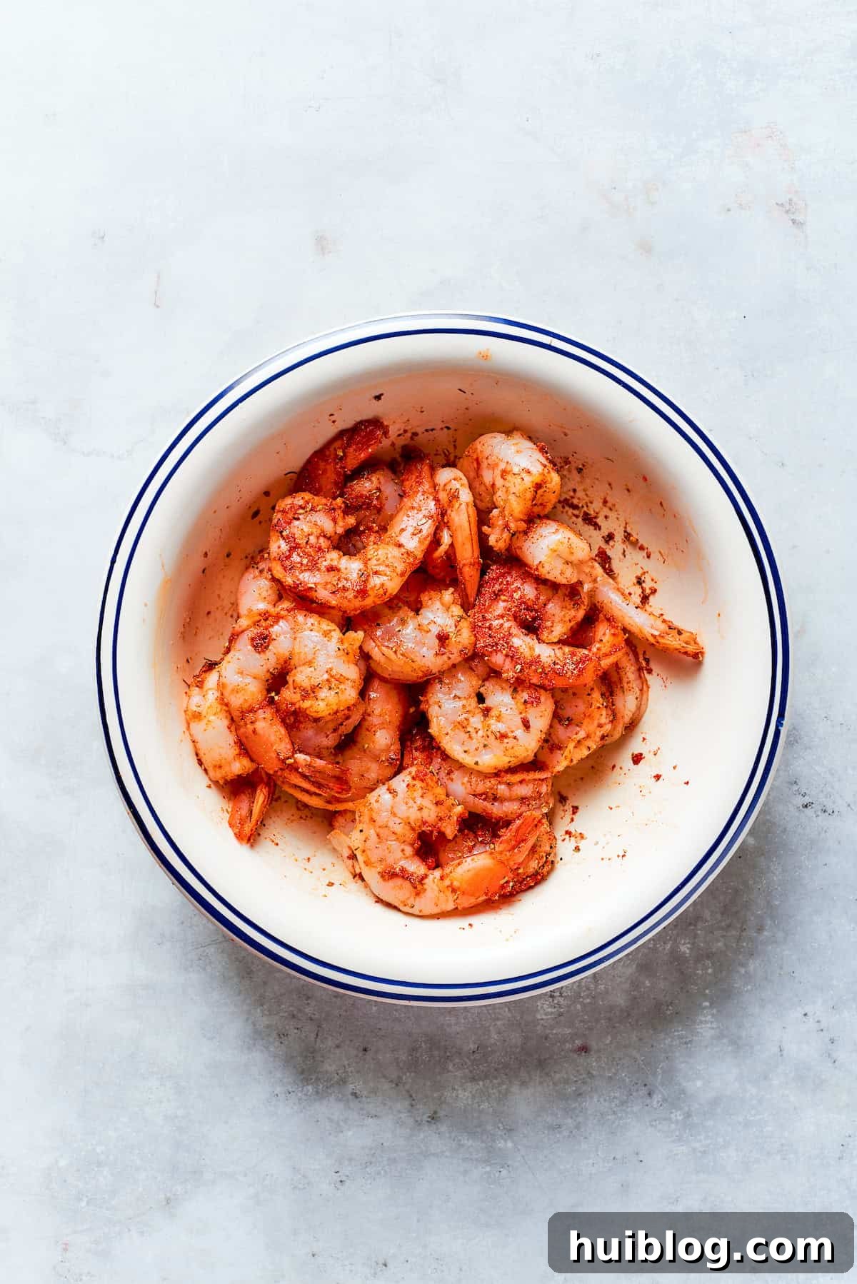 Shrimp is mixed with spices in a bowl.
