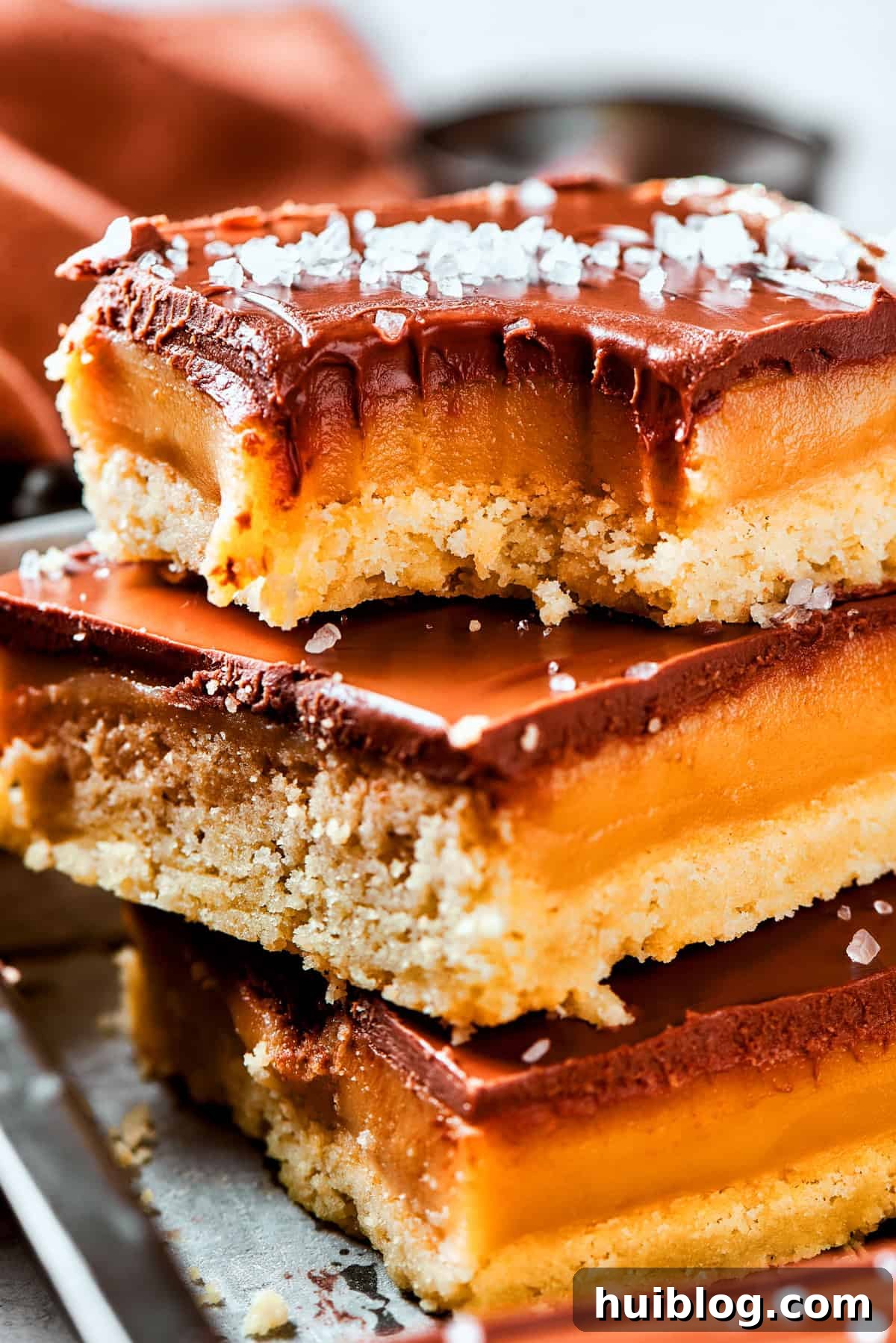 A stack of perfectly portioned Millionaire Bars, showcasing their distinct layers of shortbread, caramel, and chocolate, with a corner bite taken from the top bar.