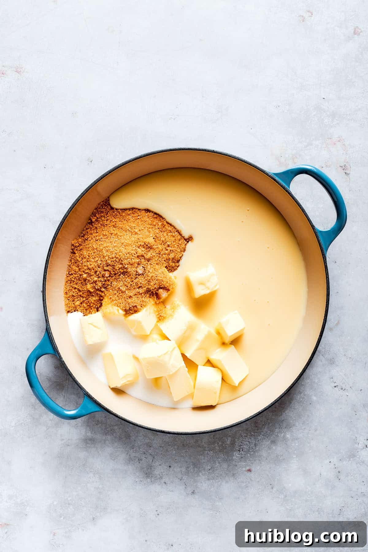 A saucepan on a stovetop, containing butter, brown sugar, condensed milk, vanilla, and heavy cream, ready to be heated for the caramel.
