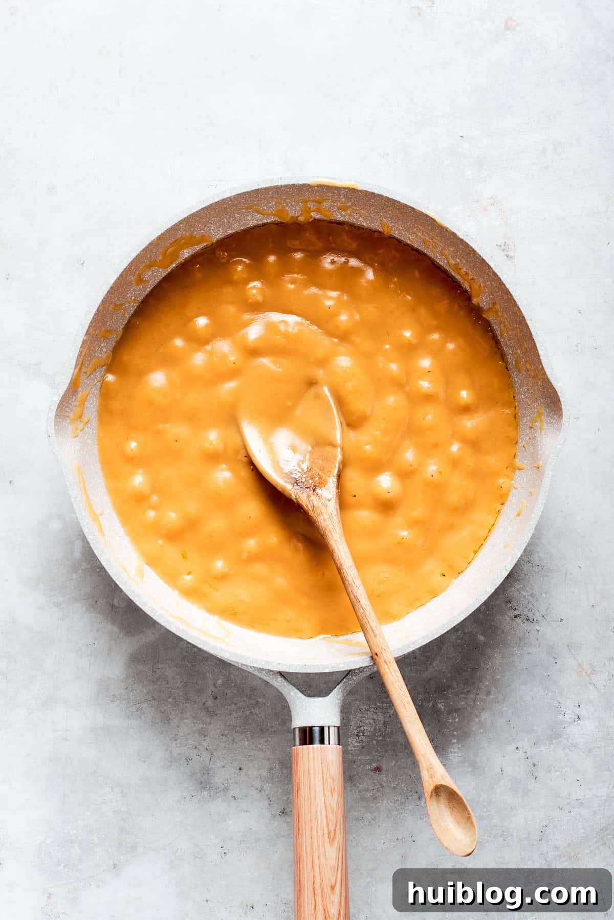 Caramel sauce is actively being stirred in a pot on the stove, appearing smooth and starting to thicken.