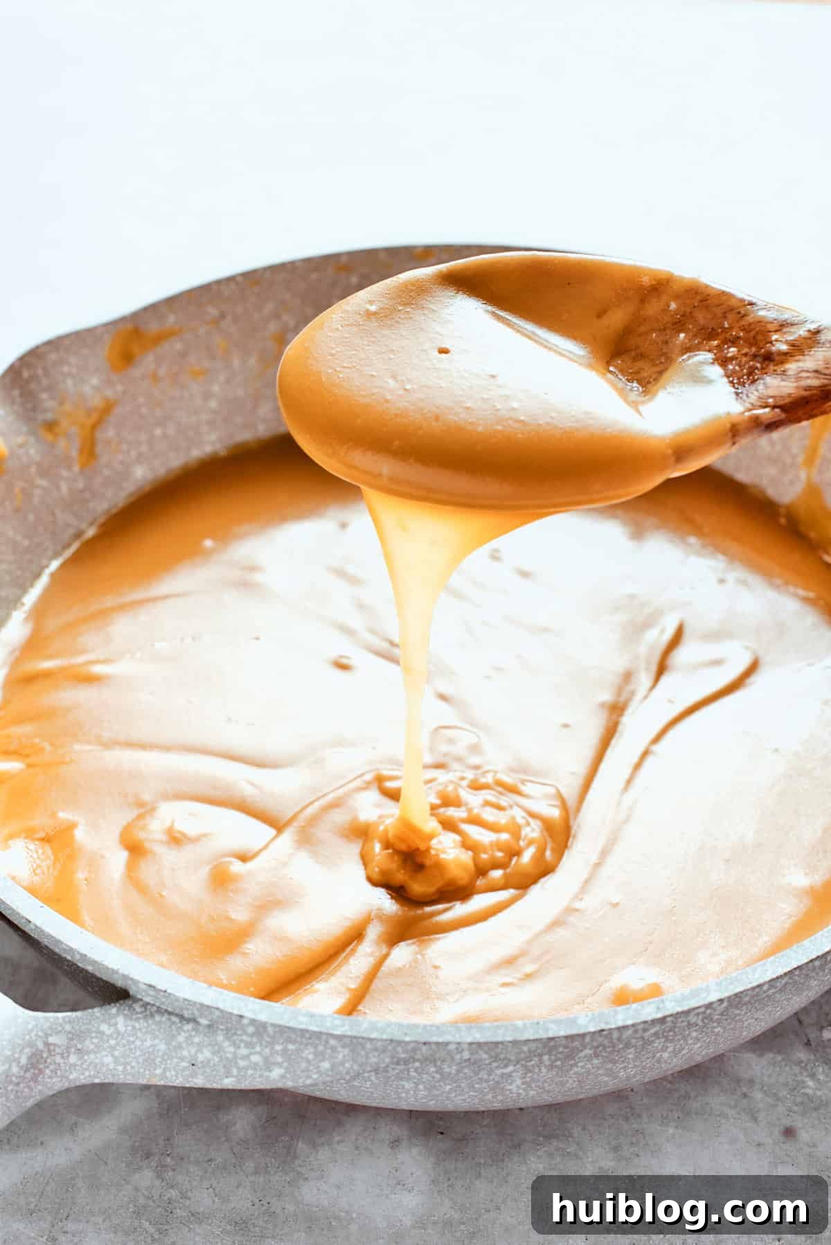 A spoon is lifting a spoonful of rich, golden caramel sauce, demonstrating its thick and smooth consistency.
