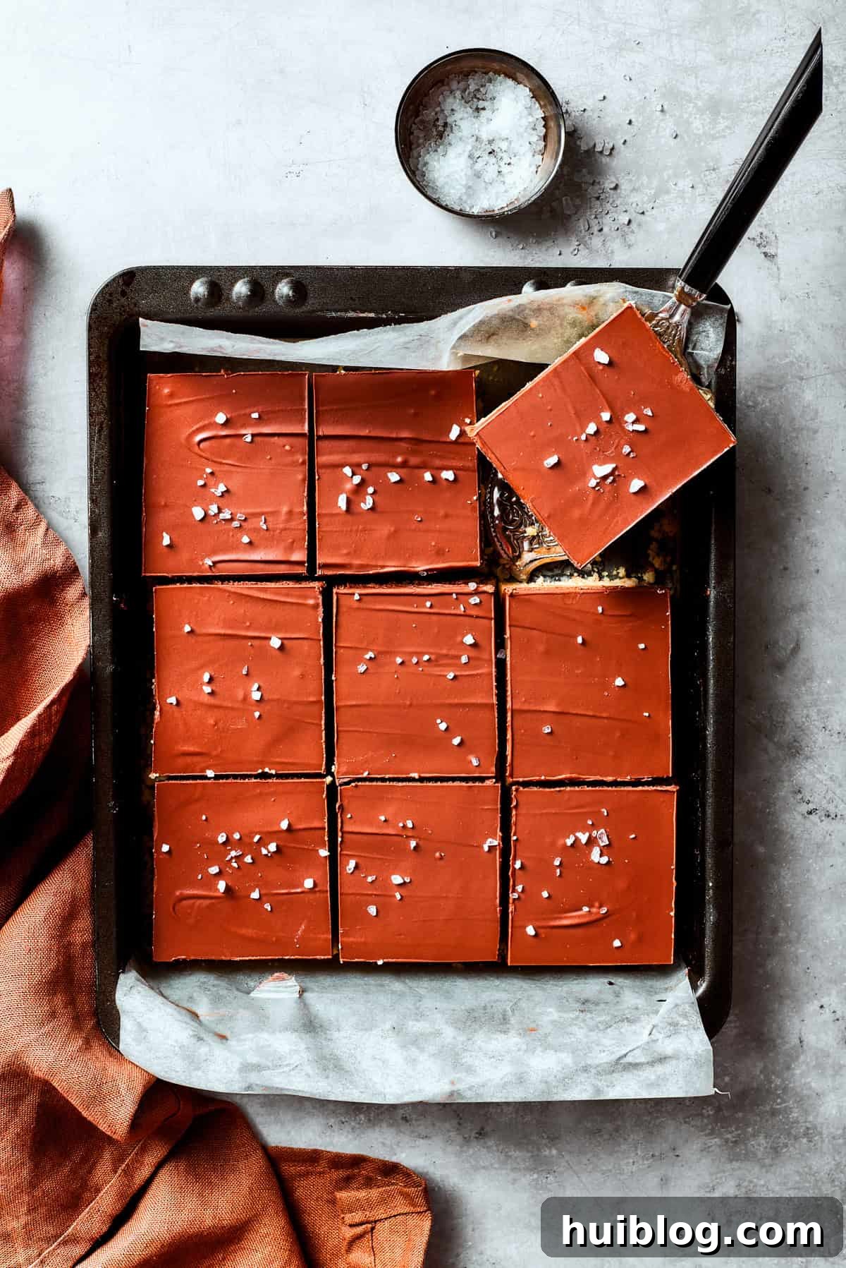 A serving utensil delicately lifts out a perfectly formed square of millionaire bar from a baking pan, ready to be enjoyed.