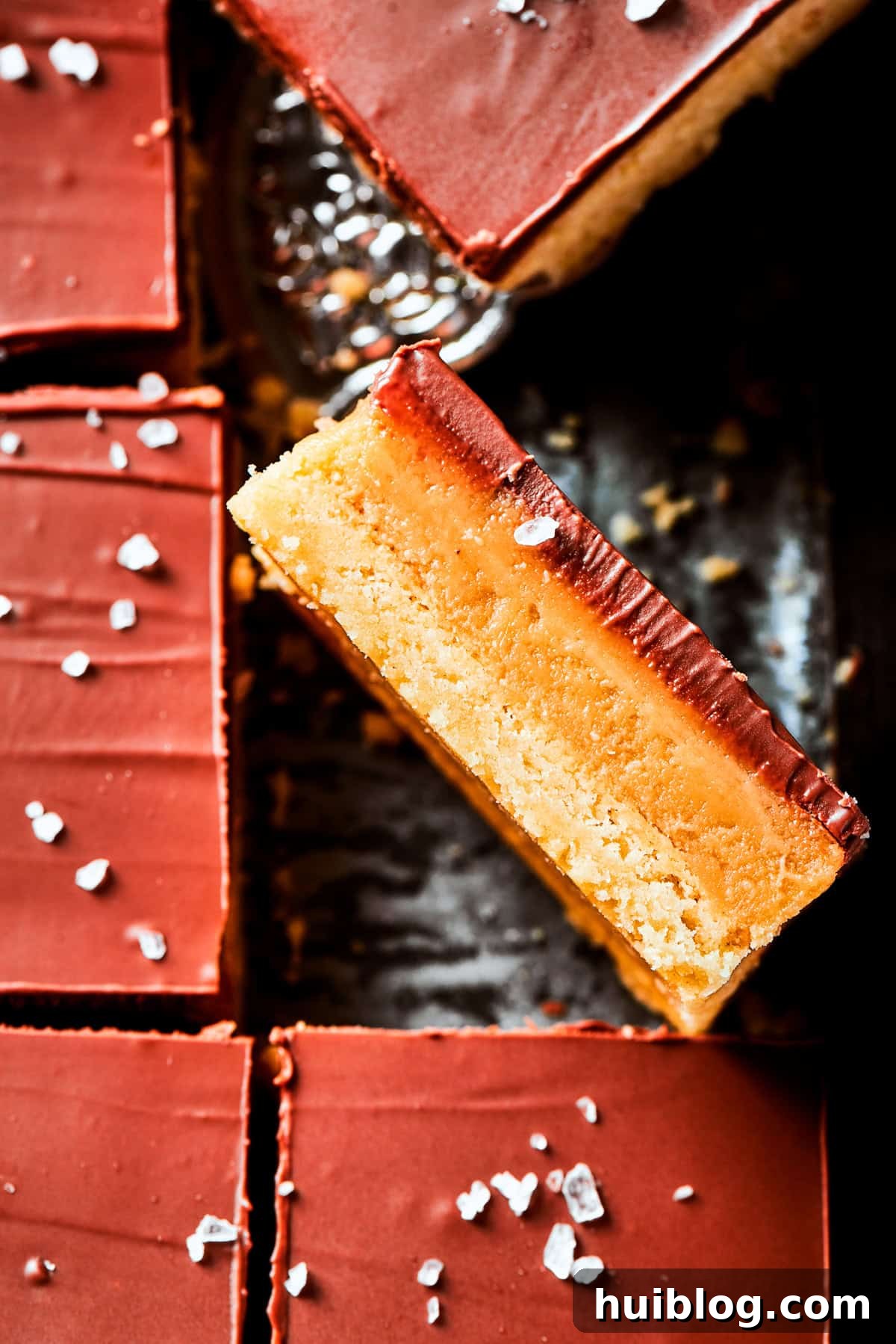 A single millionaire bar is turned on its side, resting on a pan filled with more millionaire bars, highlighting the distinct layers.