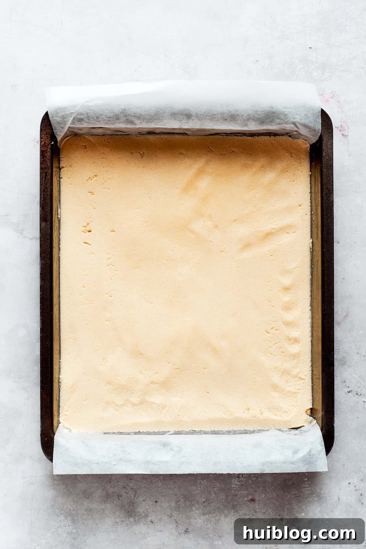The shortbread dough is being pressed into a parchment-lined baking pan, forming an even layer for the crust.