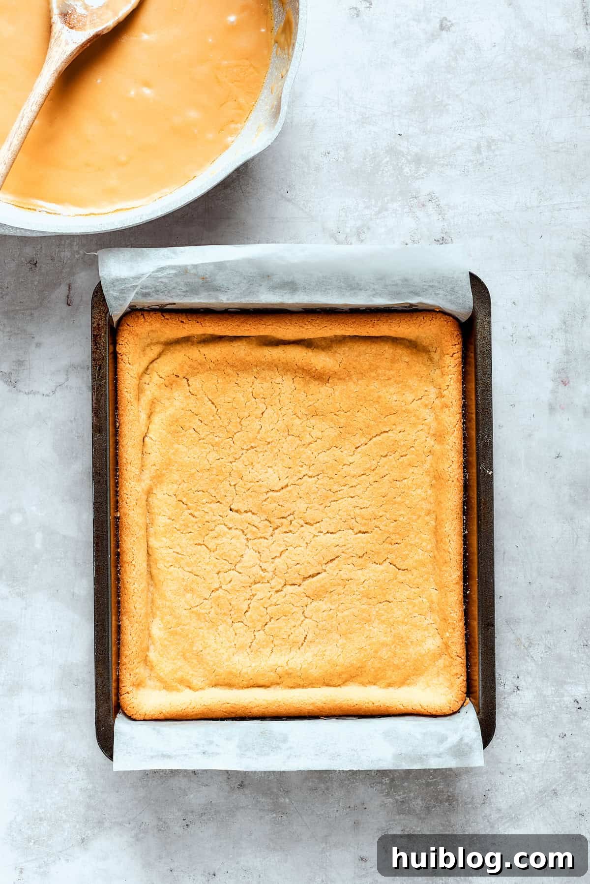 The freshly baked shortbread crust cools in the parchment-lined pan after being removed from the oven.