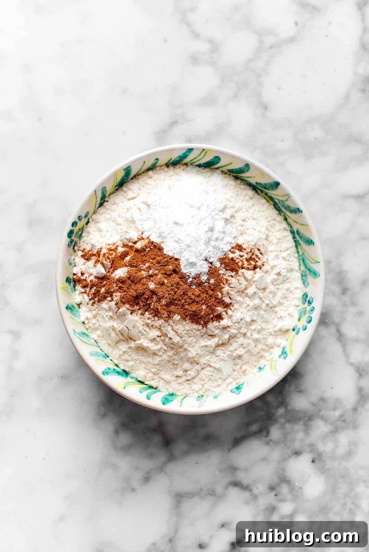 Dry ingredients like all-purpose flour, ground cinnamon, allspice, baking powder, and kosher salt being thoroughly whisked together in a spacious mixing bowl.