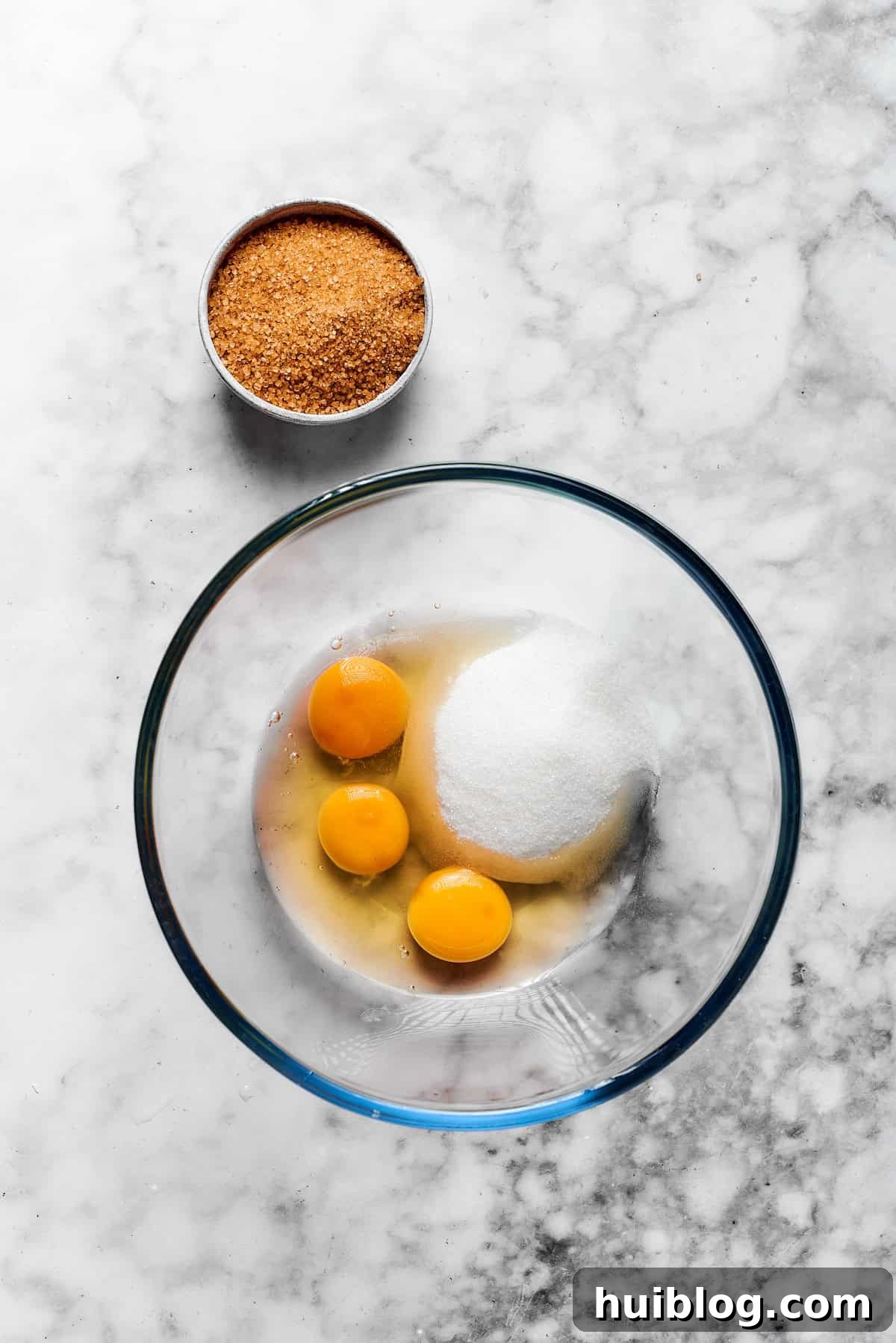 Large eggs, granulated sugar, and light brown sugar being beaten together in a separate bowl until the mixture is smooth and evenly combined.