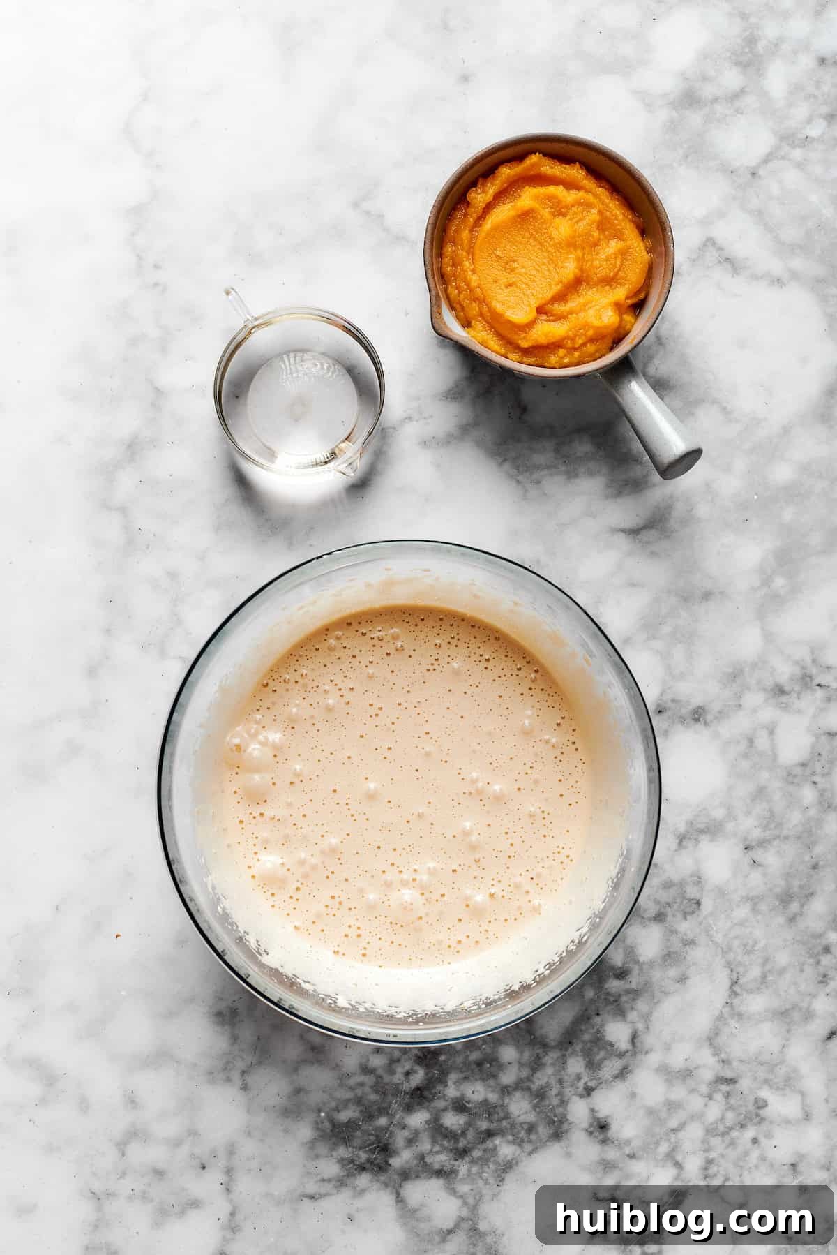 Pumpkin puree and vegetable oil being gently stirred into the previously combined egg and sugar mixture until fully integrated and creamy.