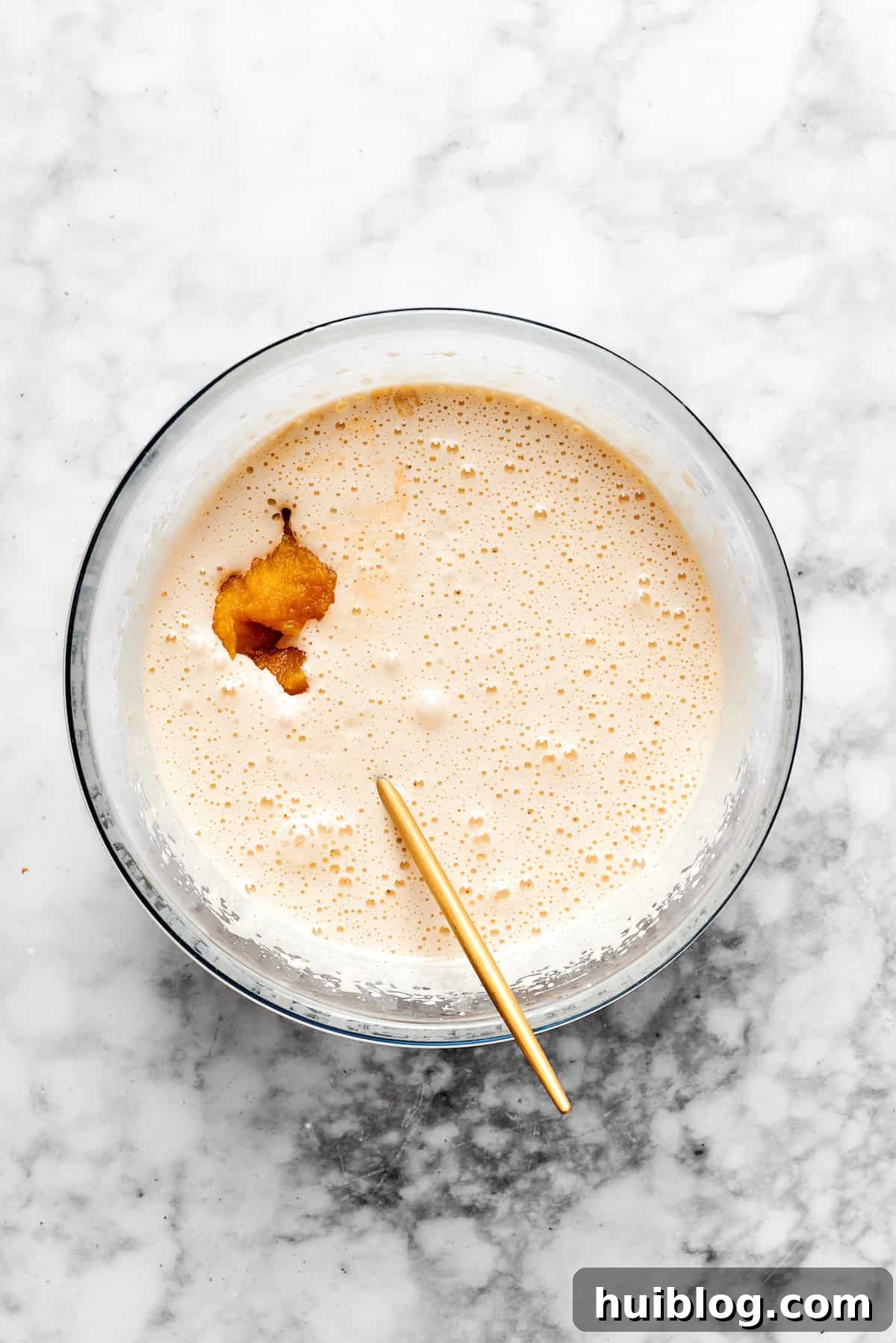 A measured amount of pure vanilla extract being poured into the wet pumpkin muffin batter, ready to enhance the overall flavor.
