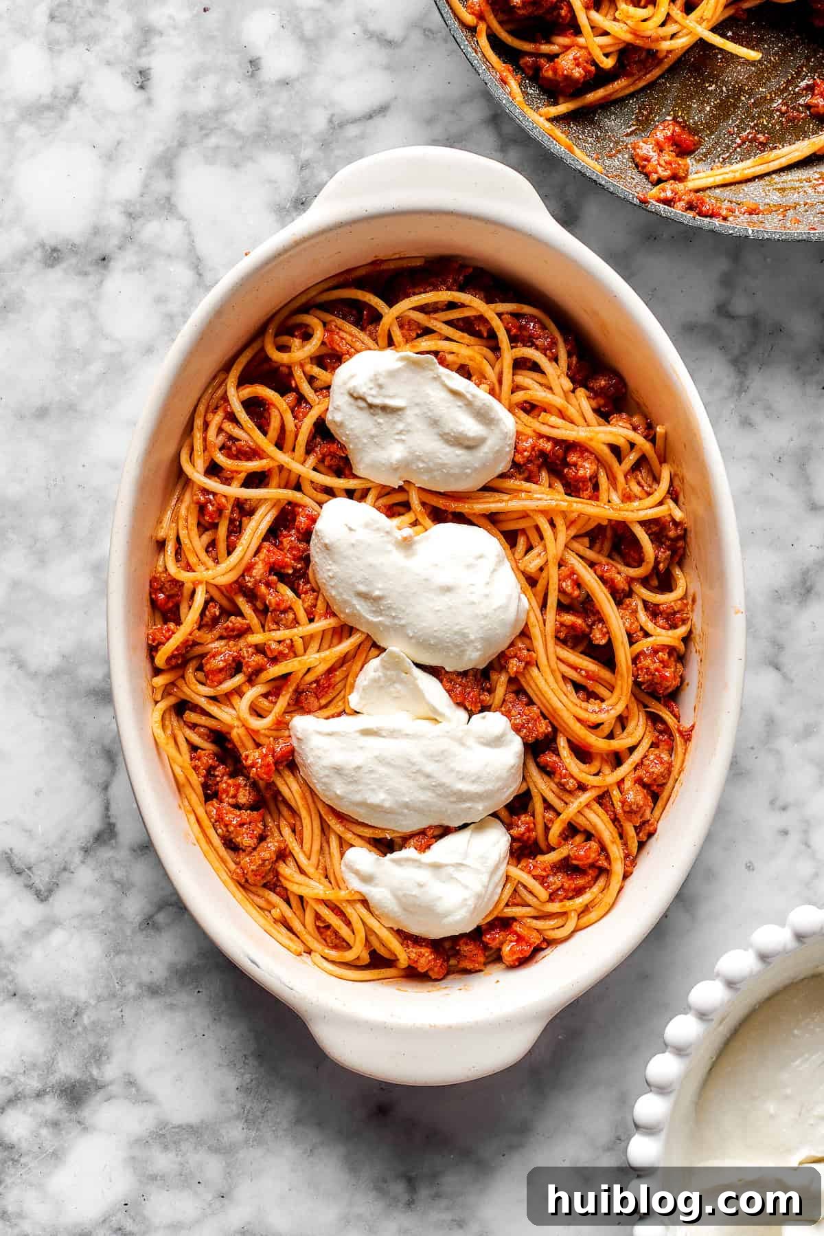 Adding cheese mixture on top of spaghetti and meat sauce in a baking dish.