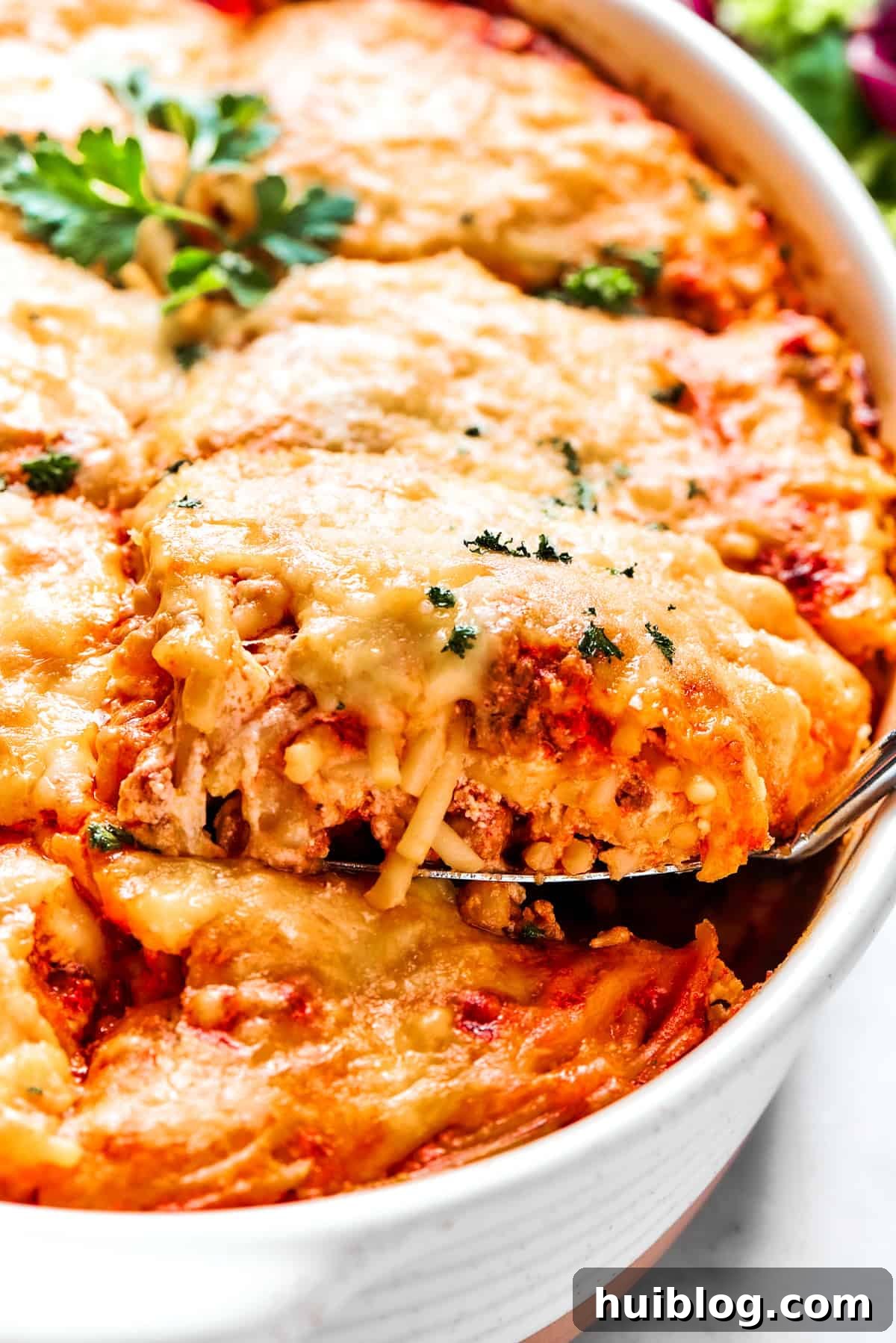 Spooning out baked spaghetti from a casserole dish, showing the layers of pasta, sauce, and cheese.