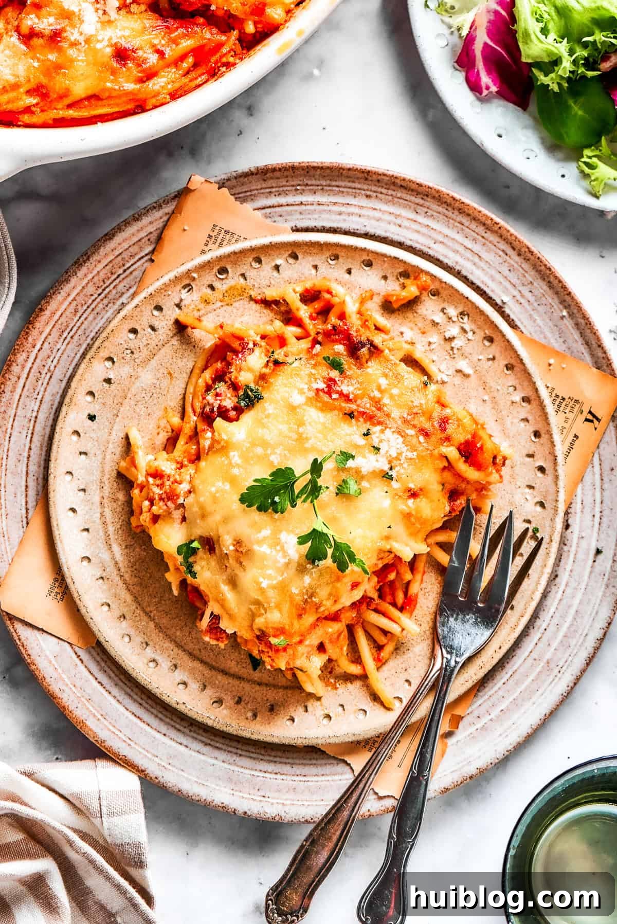 A serving of million dollar spaghetti, scooped onto a plate with forks, ready to eat.