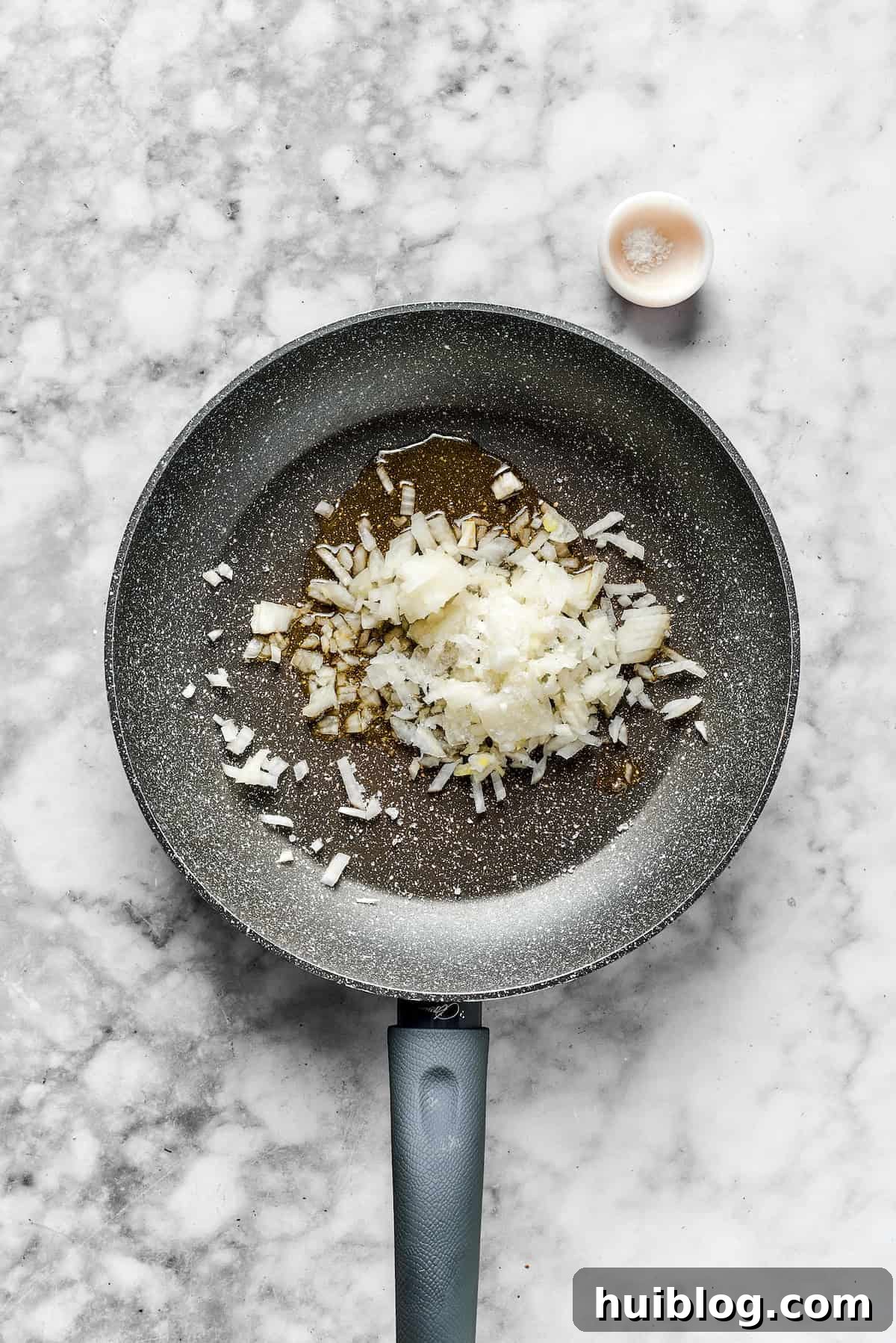 Diced onions in a skillet, ready to be cooked.