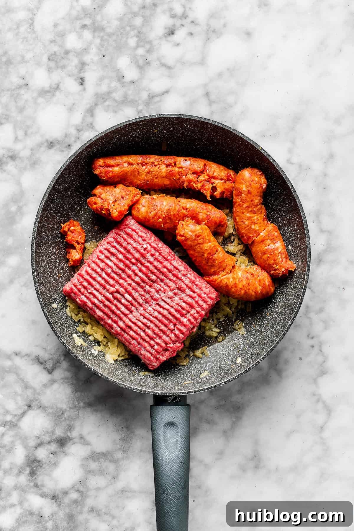 Adding ground beef and sausage to the skillet with cooked onions.