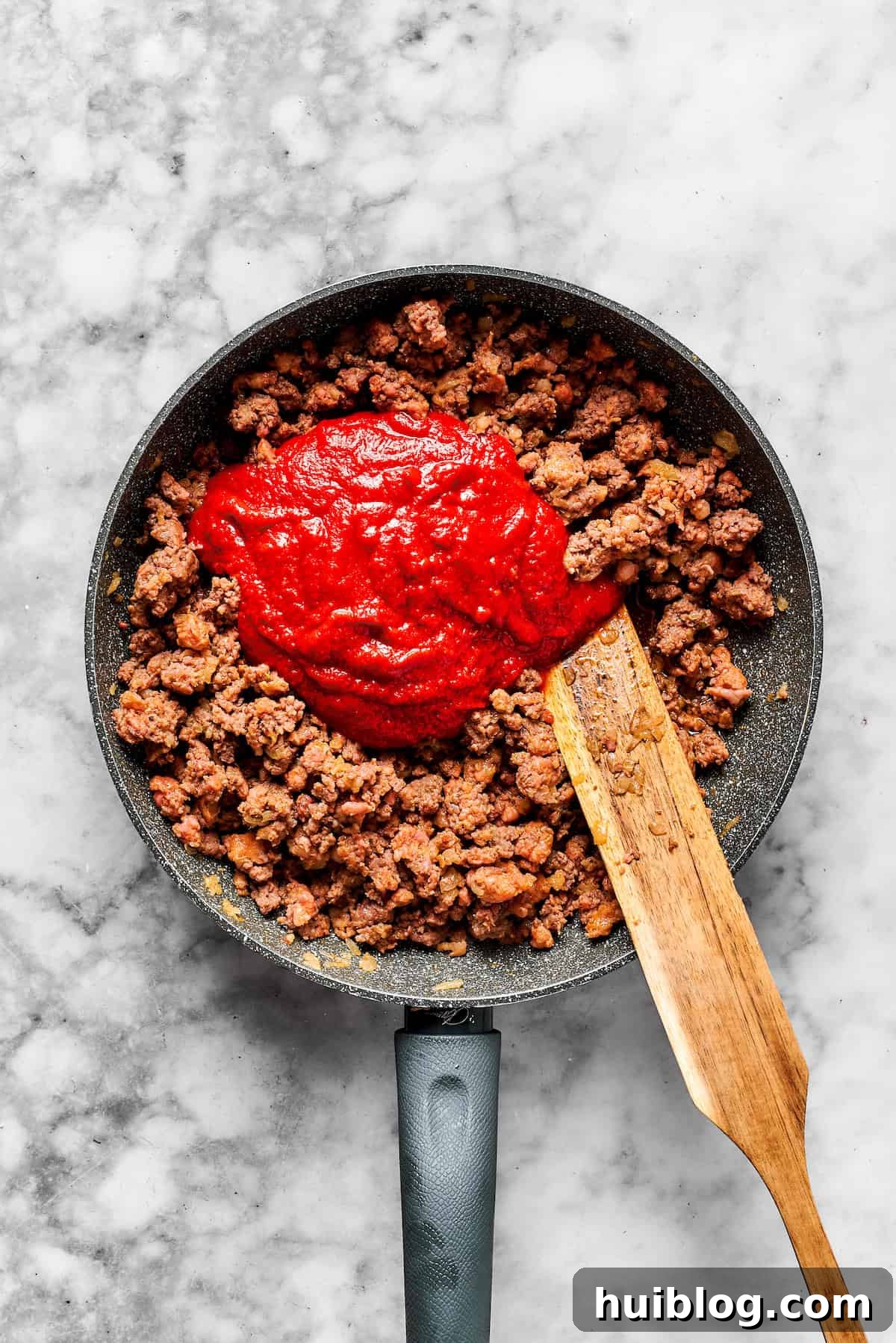 Adding pasta sauce to a skillet with cooked meat and seasonings.