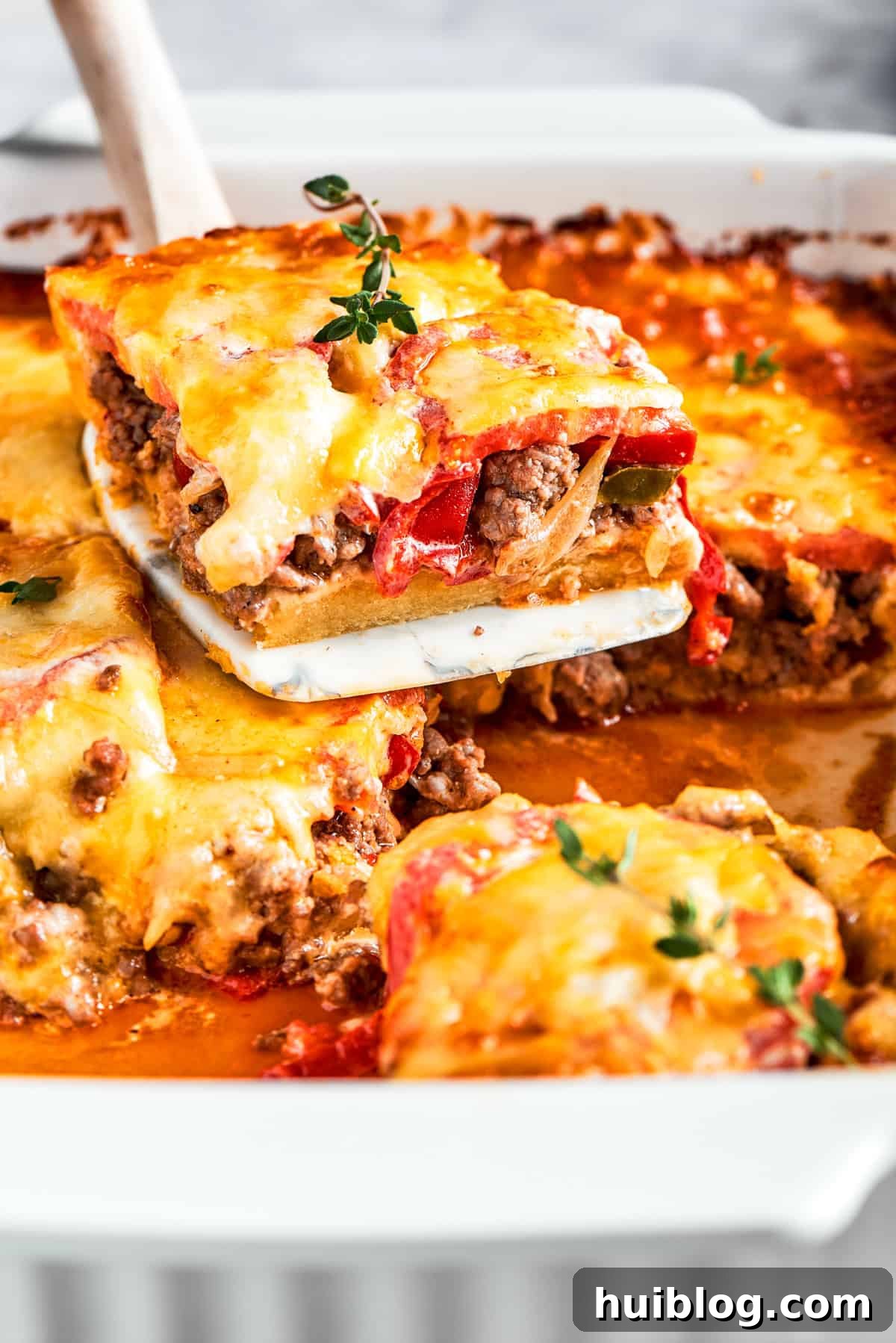 A slice of John Wayne Casserole being lifted out of the baking dish, showing layers of biscuit, meat, and cheese.
