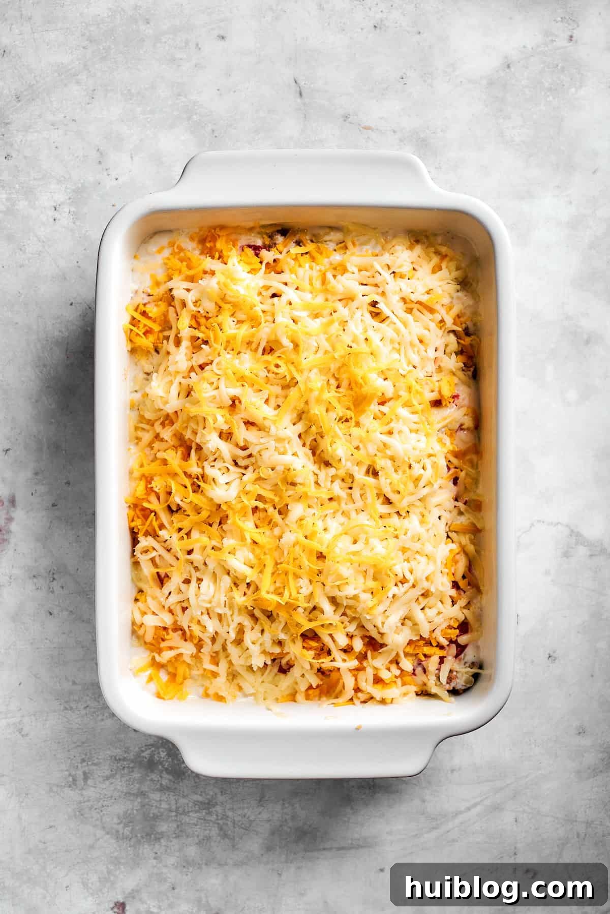 Cheddar and mozzarella cheese sprinkled over the sour cream layer, ready for baking.