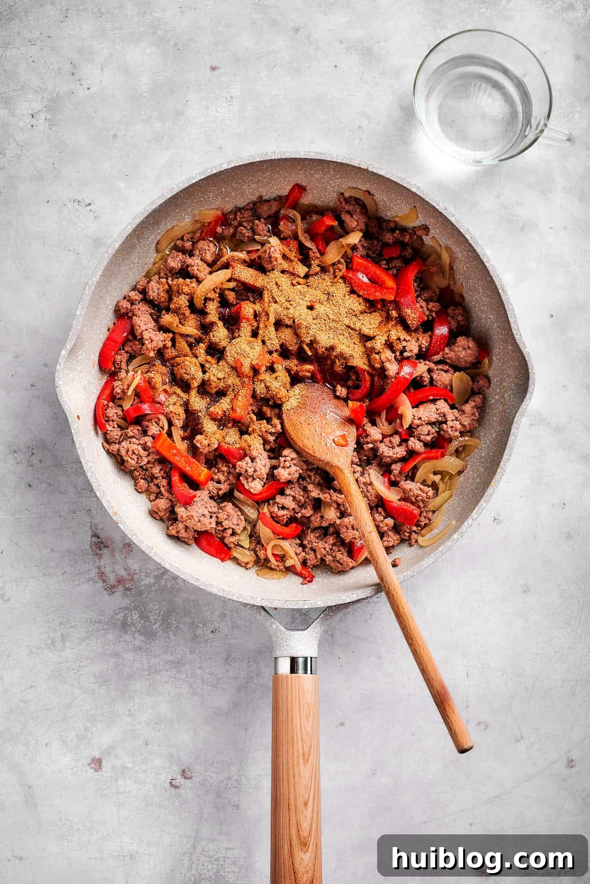 Sprinkling taco seasoning over cooked ground beef and vegetables in a skillet.